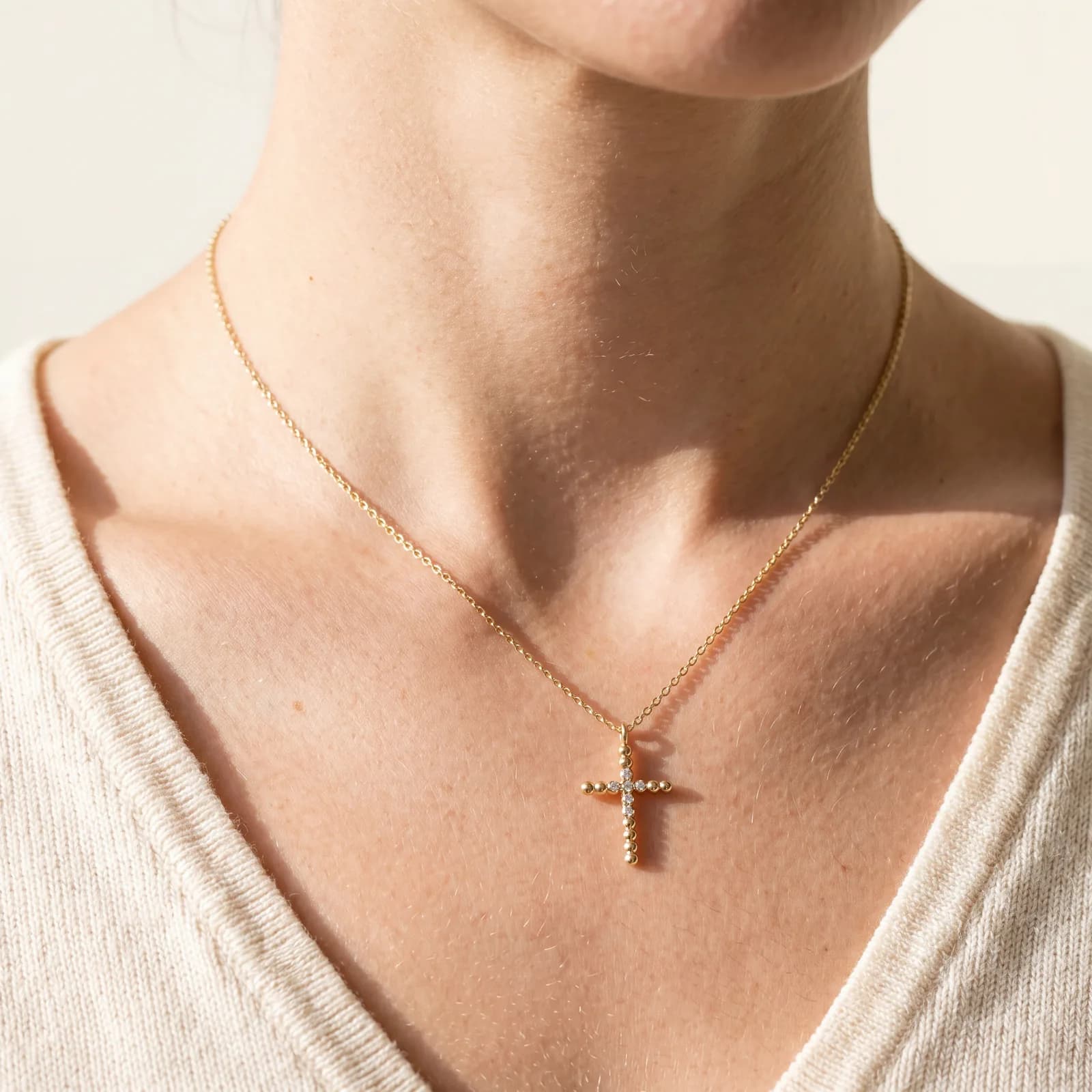 A close view of a neck and chest wearing a gold chain with a beaded gold cross pendant set with small diamonds.