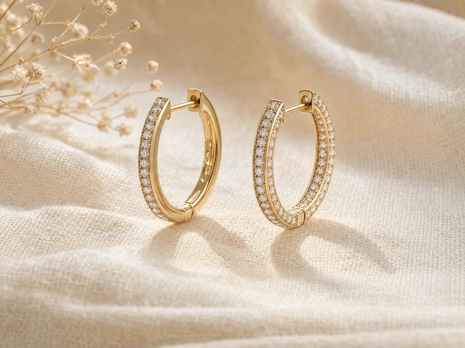 A front-facing pavé diamond hoop earring beside an inside-outside diamond hoop earring on a woven cream linen surface, showing the difference in diamond coverage between the two settings.