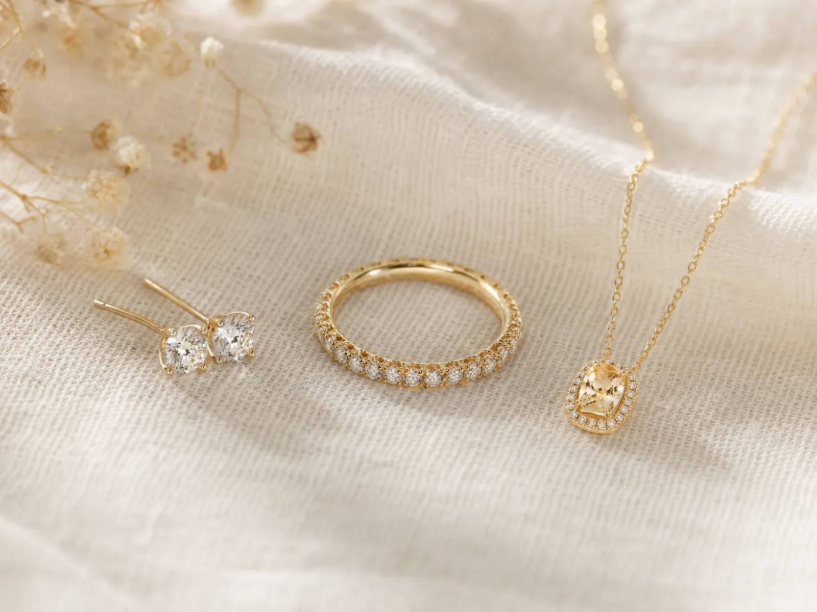Diamond stud earrings, an eternity band, and a birthstone pendant arranged together on woven cream linen — three of the five most popular push present categories.