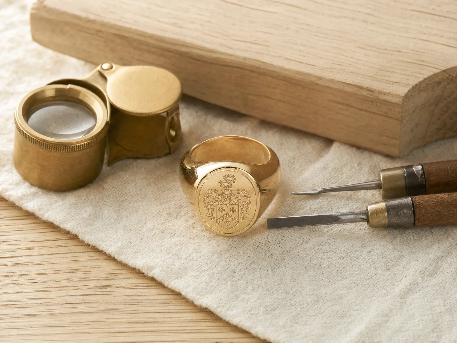 A heavy gold signet ring on a jeweler's workbench with a brass loupe and engraving tools at ATL Luxury Jewelry's Snellville atelier