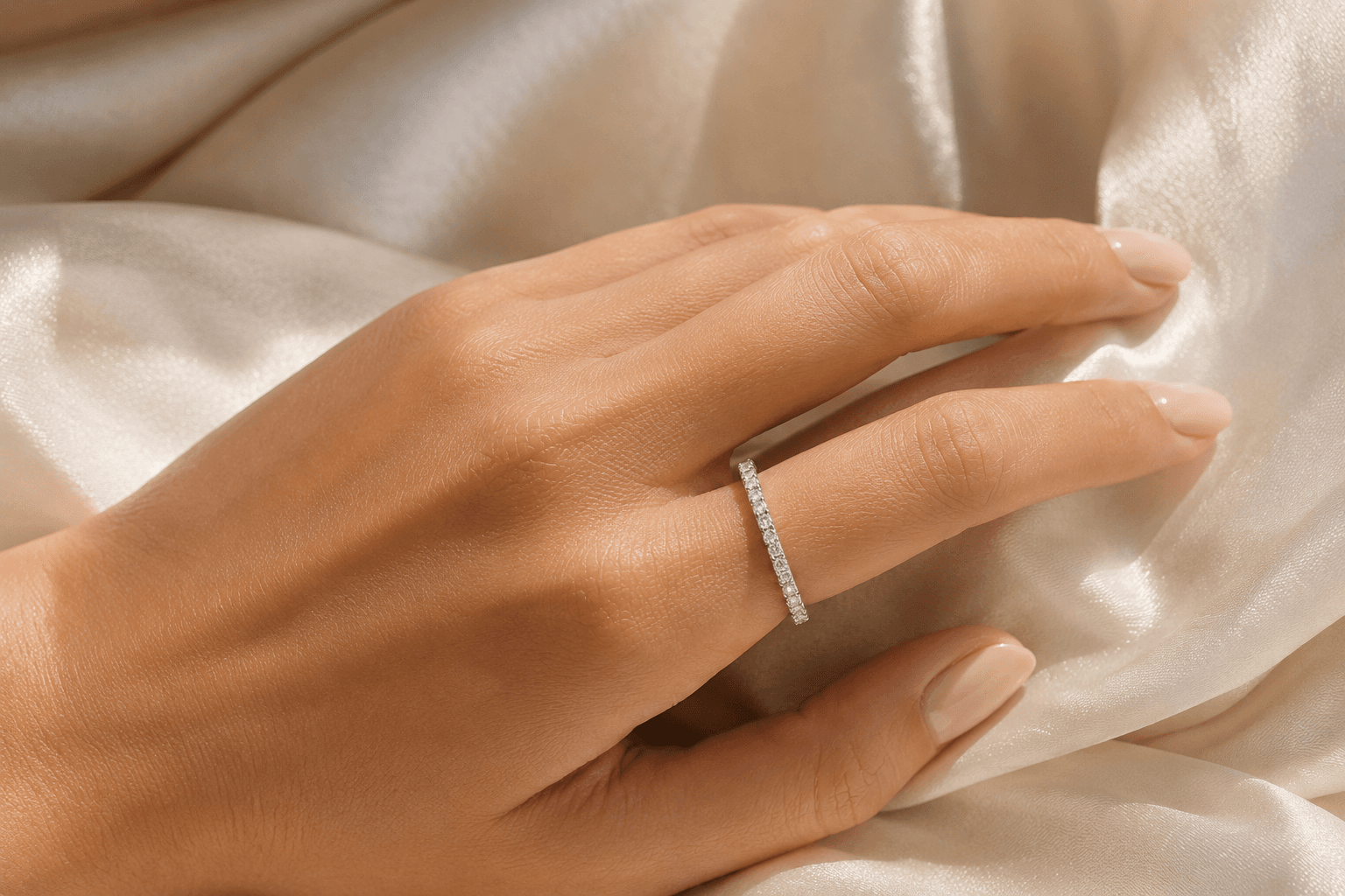 Diamond eternity wedding band on a woman's hand resting on cream silk