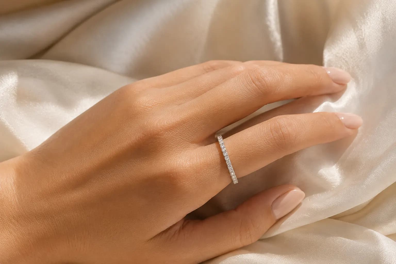 Diamond eternity wedding band on a woman's hand resting on cream silk