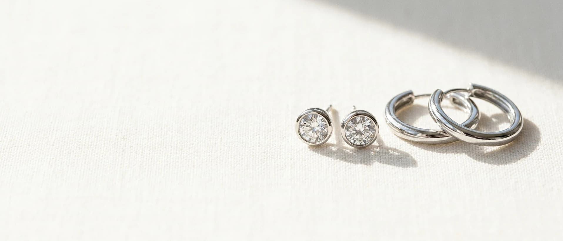 White gold diamond stud and hoop earrings on cream linen at ATL Luxury Jewelry Atlanta