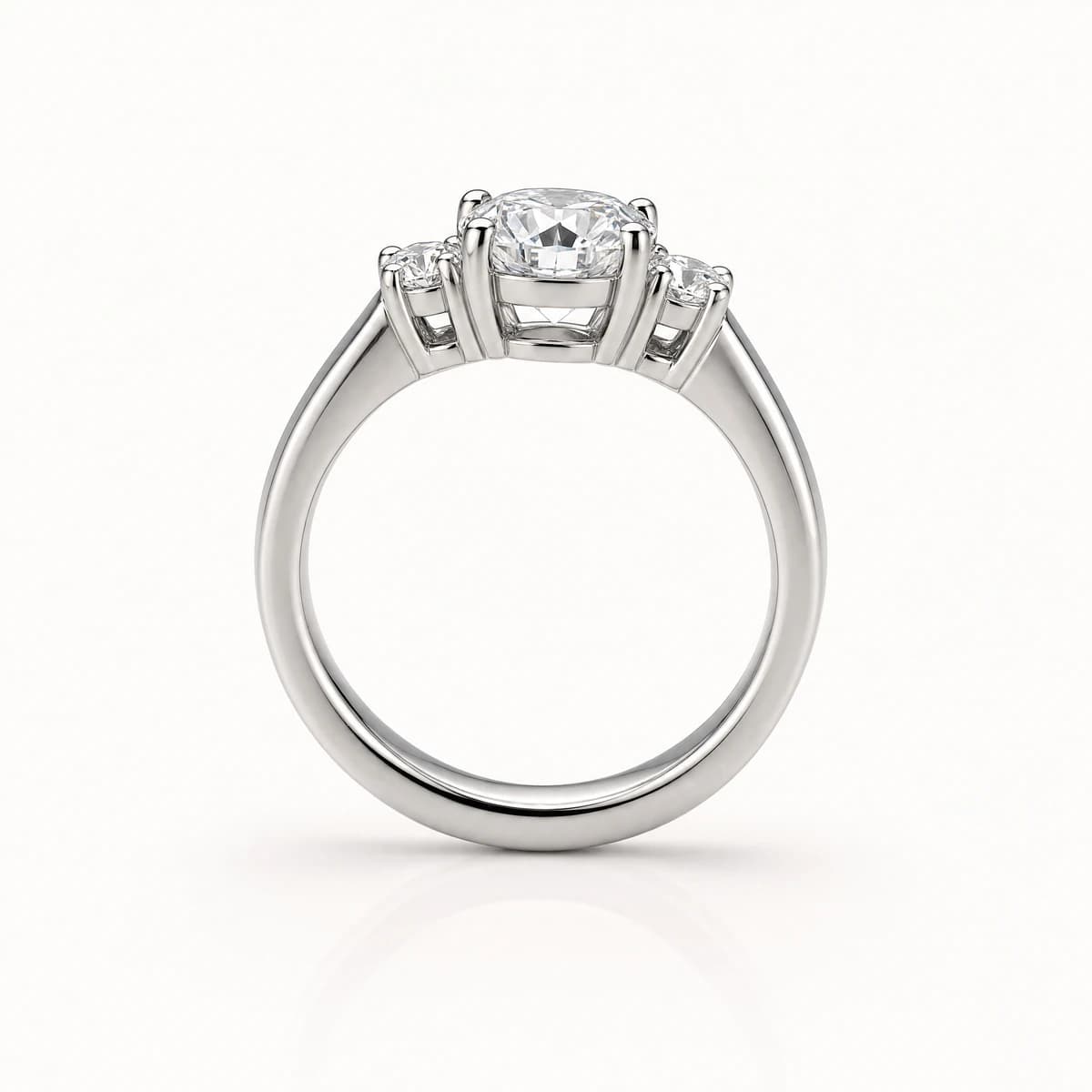 A platinum three-stone ring standing upright on a pale background, a round brilliant centre diamond flanked by two smaller round side stones