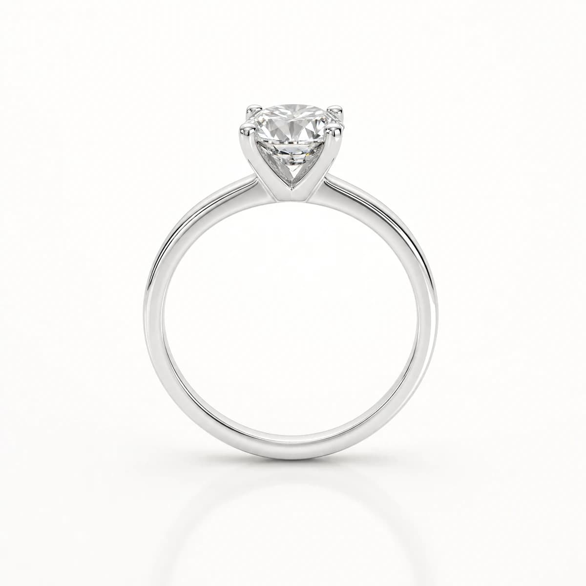 A white gold solitaire ring standing upright on a pale background, one round brilliant diamond held in four prongs on a plain polished band
