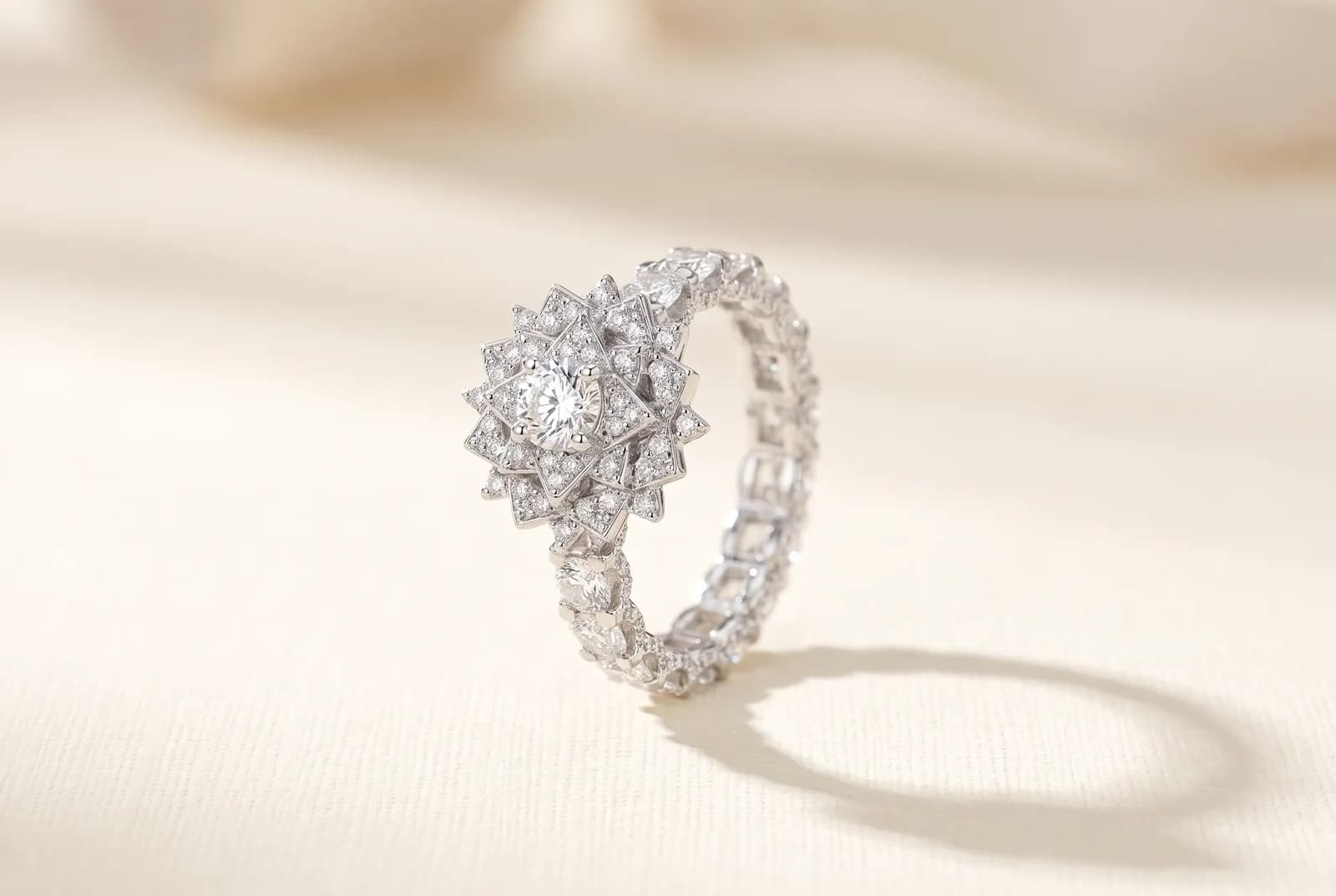A design study for a white metal ring on a cream surface: a round brilliant diamond inside a pointed starburst halo of smaller diamonds, on a band set edge to edge with pave diamonds all the way around