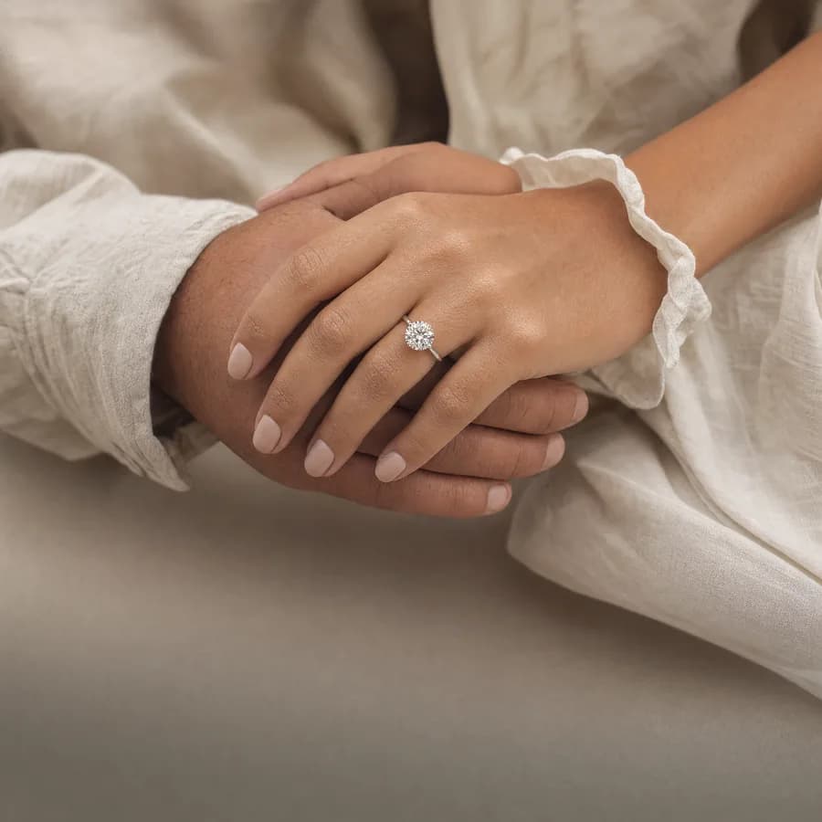 Couple's hands clasped, showing a 2 carat round diamond engagement ring