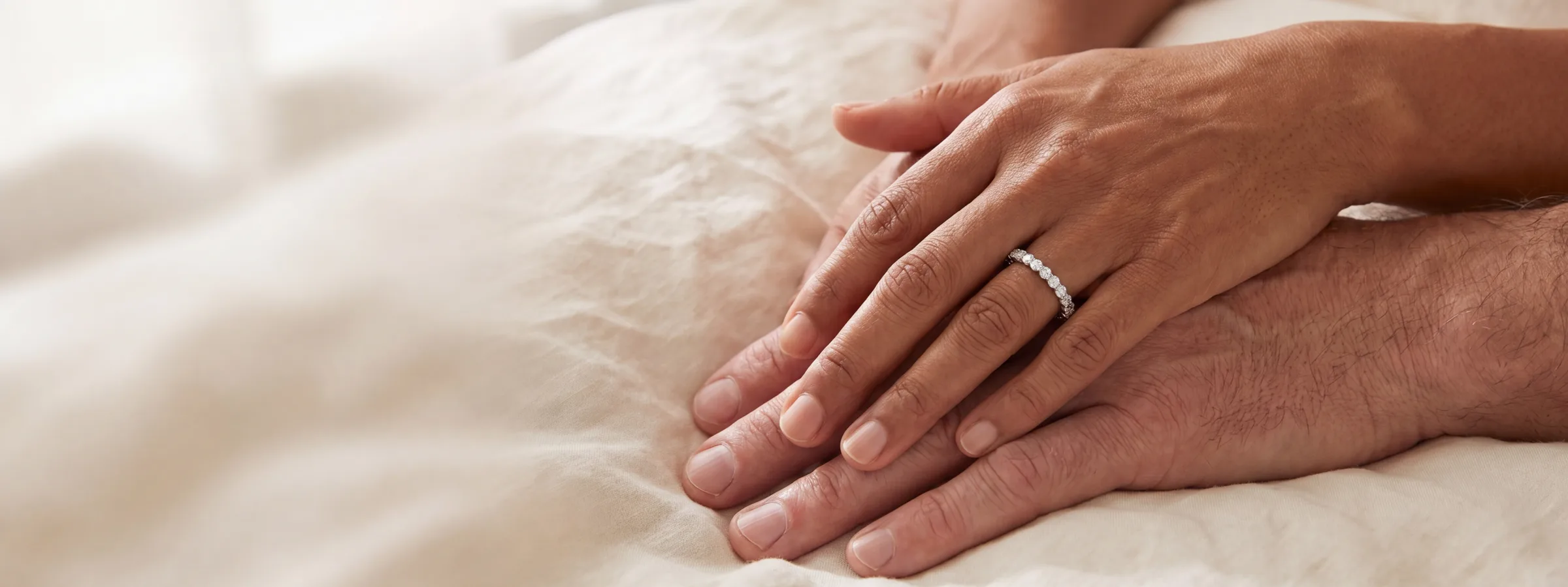 A close-up of hands wearing anniversary jewelry, resting against neutral fabric.