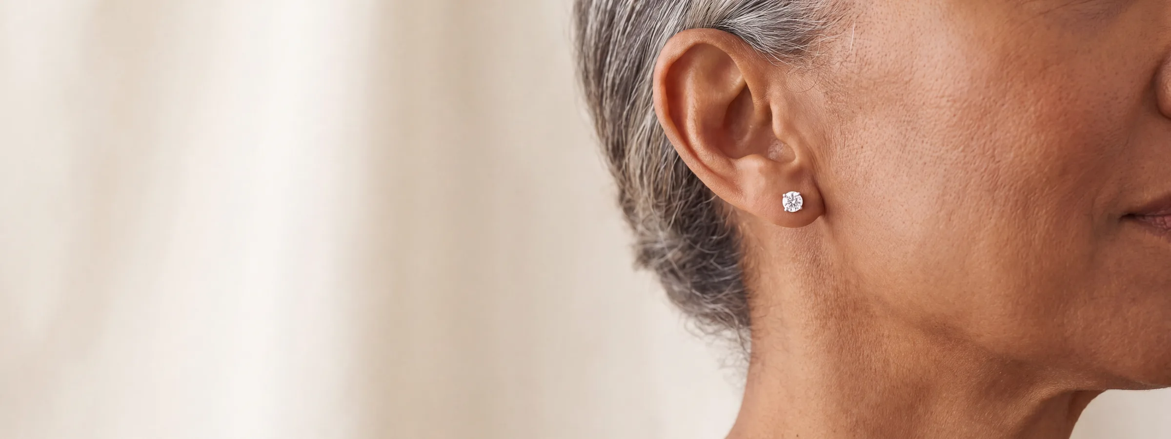 A close-up of a woman's ear wearing a single round diamond stud earring.