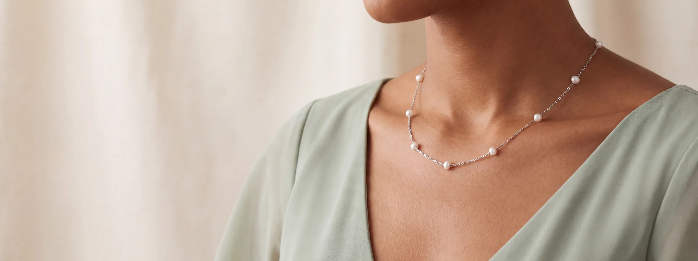 A pearl station necklace worn at the neckline, over a sage green top