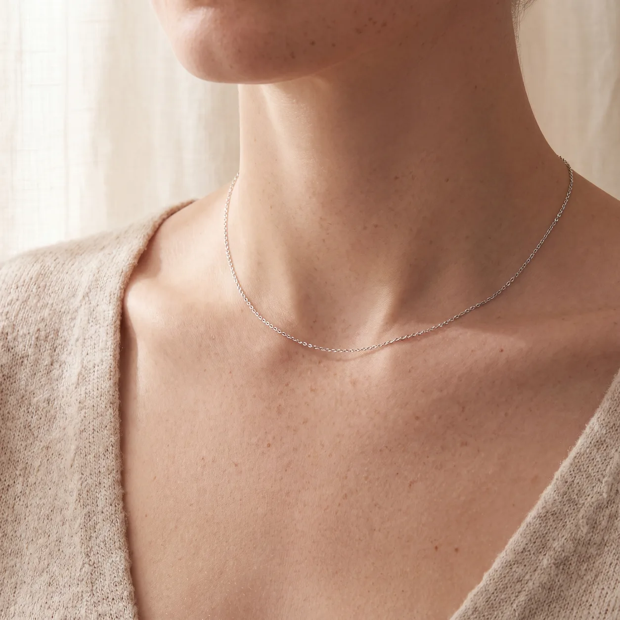 A woman wearing one thin silver chain necklace resting at the collarbone, seen close up