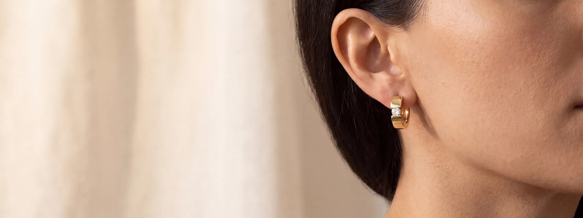 A small gold huggie hoop earring worn in the ear