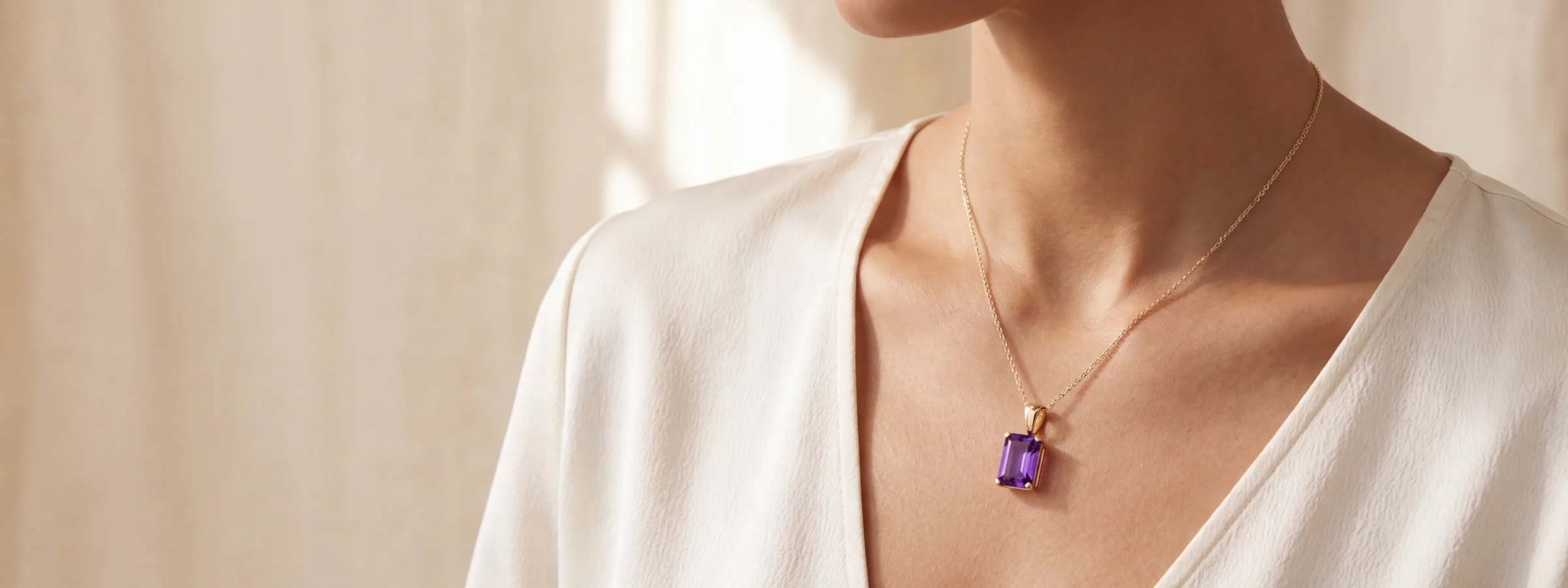 An emerald-cut amethyst pendant on a fine gold chain, worn at the collarbone over a white top