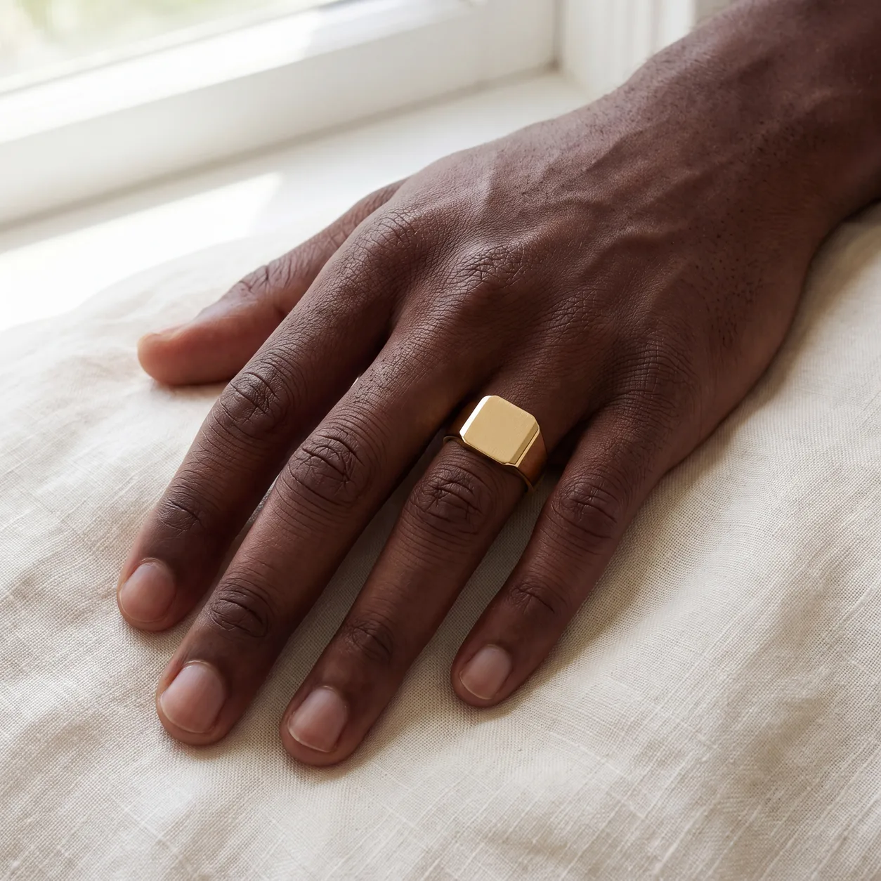 A men's gold link bracelet and a silver cuff bracelet laid together on cream fabric
