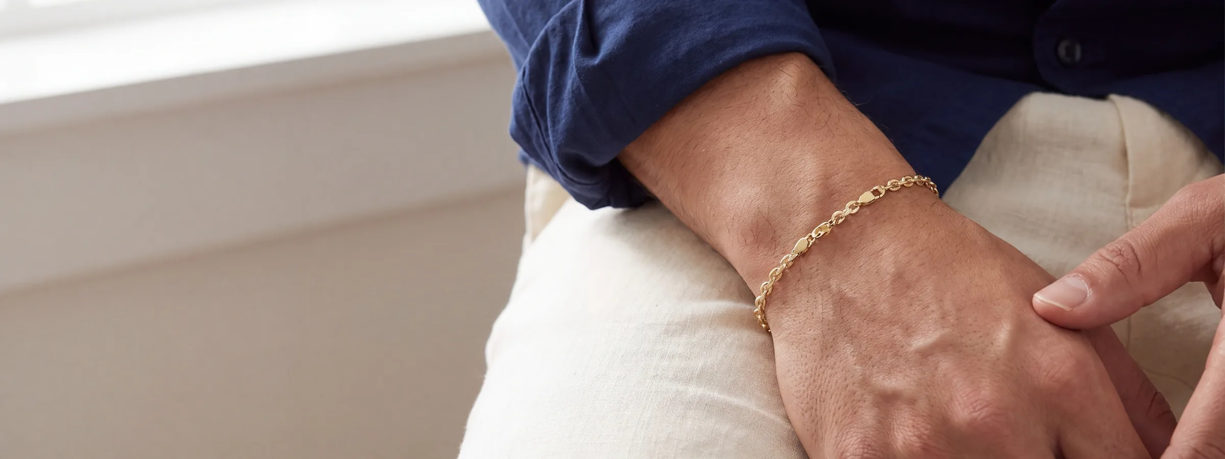 A wrist resting on a knee, wearing a gold link bracelet