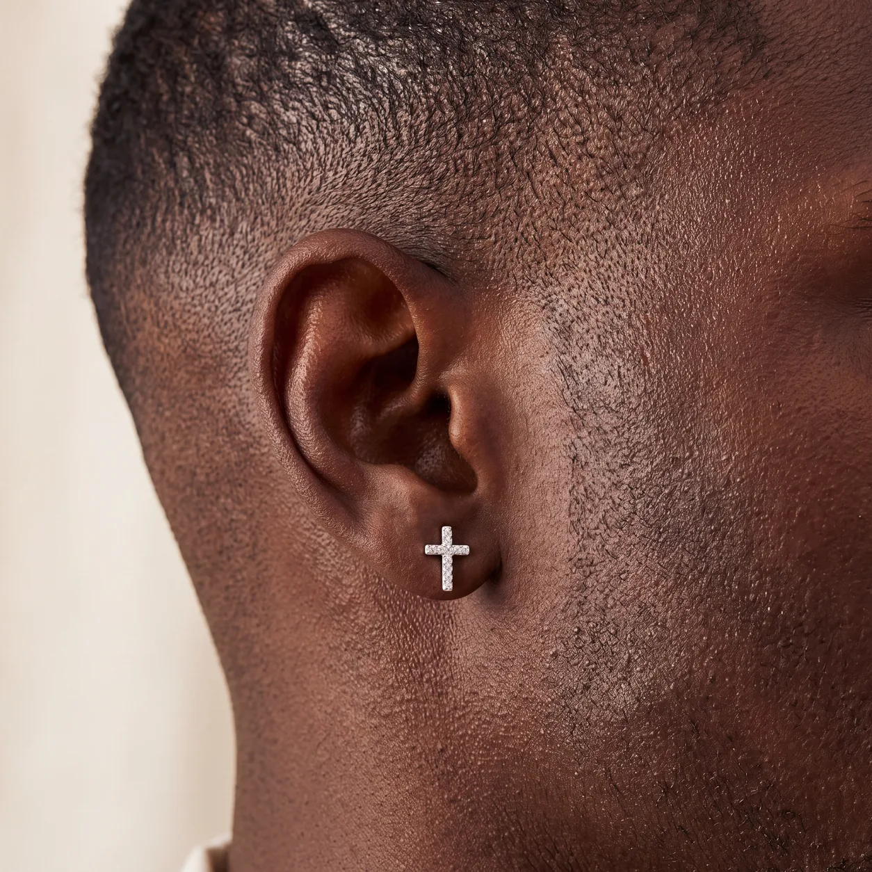 A small diamond cross stud earring on a man's ear