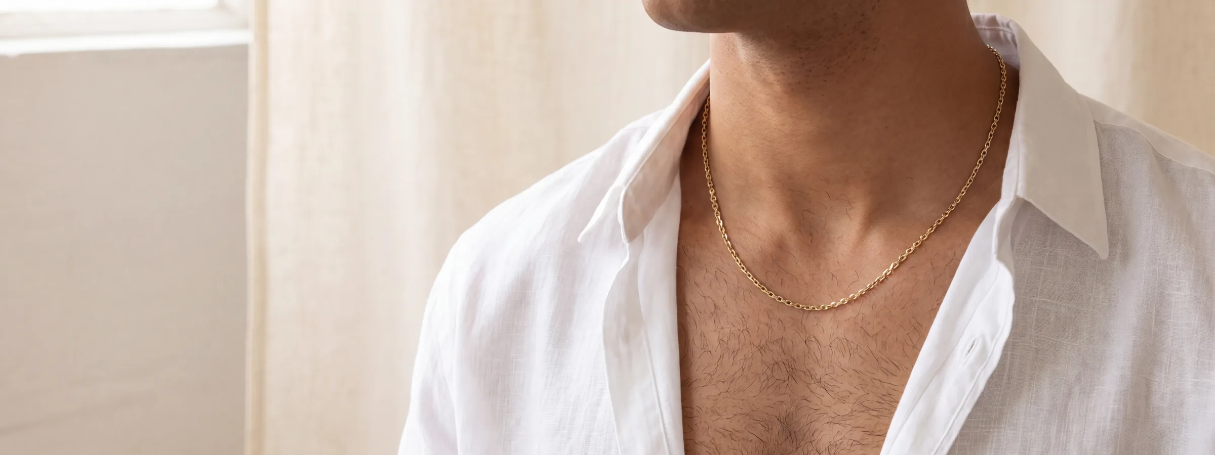 A fine gold chain worn at the neck, open at the collar of a white linen shirt