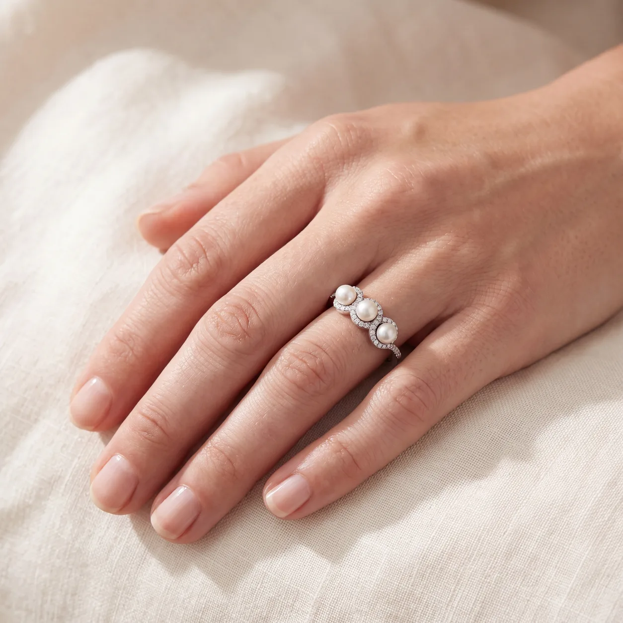 A hand wearing a ring set with three pearls in a diamond pave band