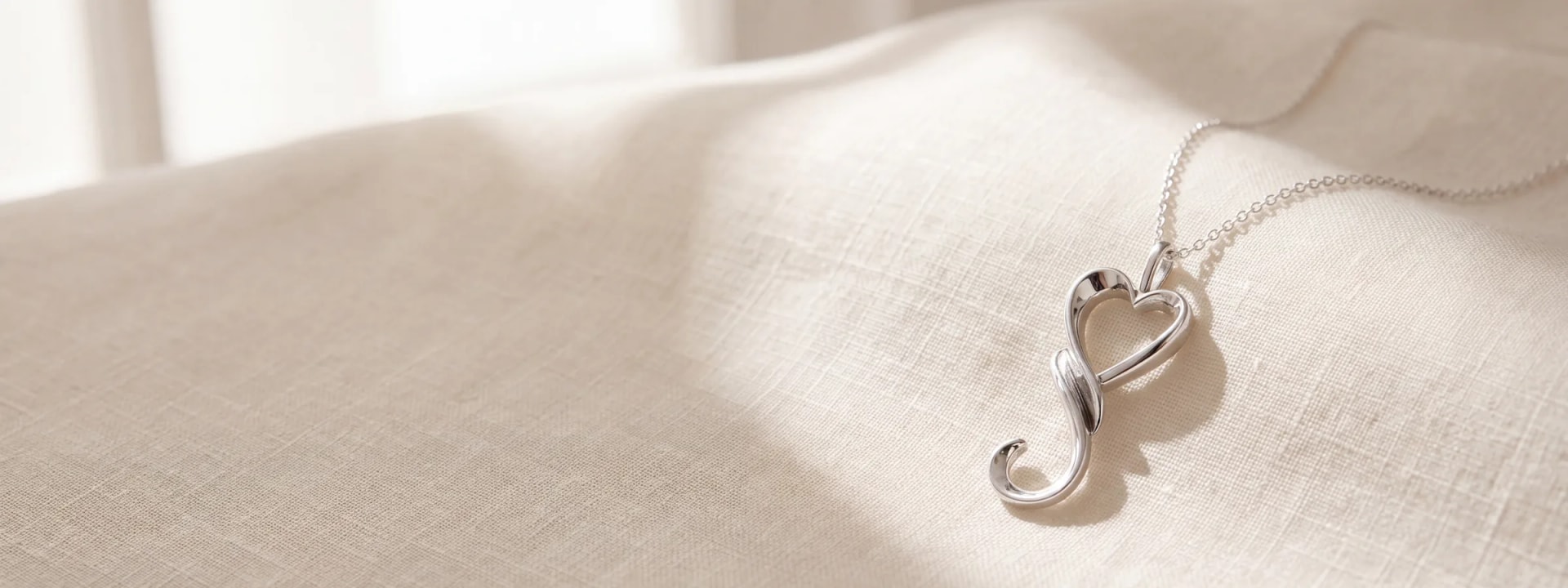 A silver heart pendant necklace resting on cream linen