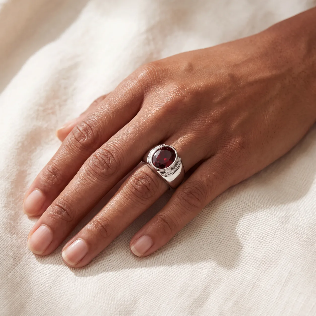 A hand wearing a ring set with a large oval red stone in a diamond-accented band