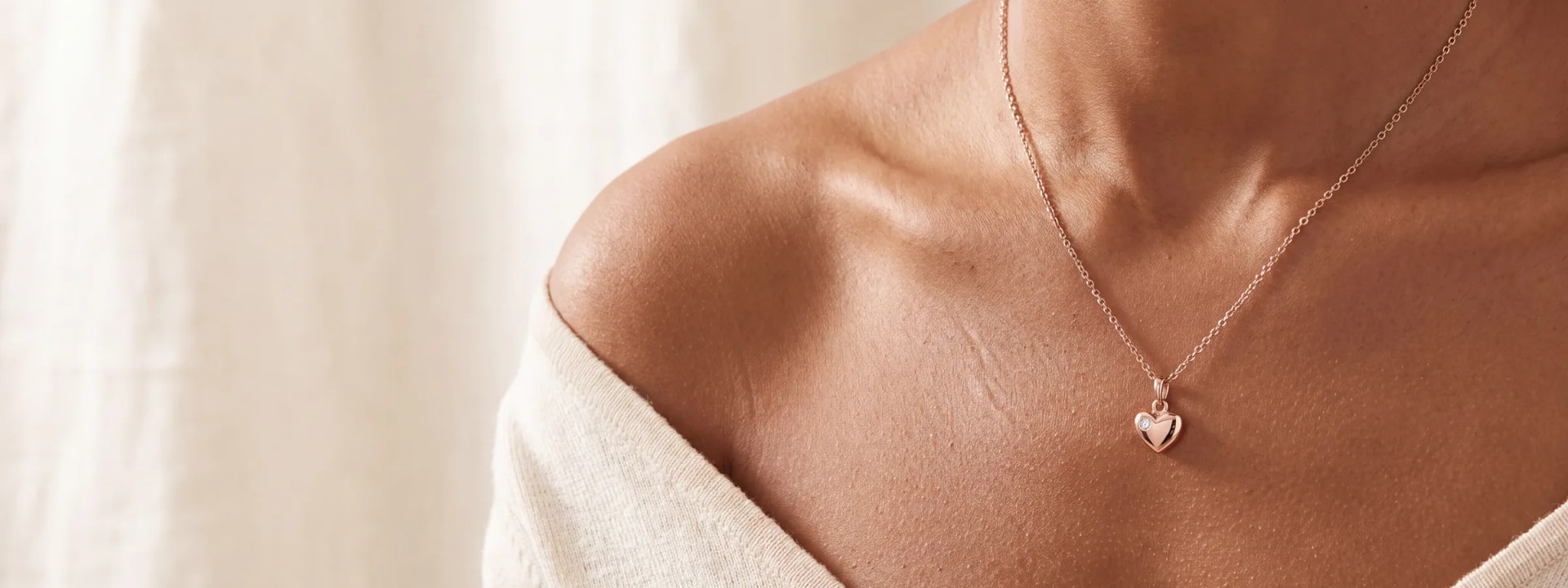 A woman's collarbone and shoulder wearing a rose gold heart pendant necklace with a small diamond accent