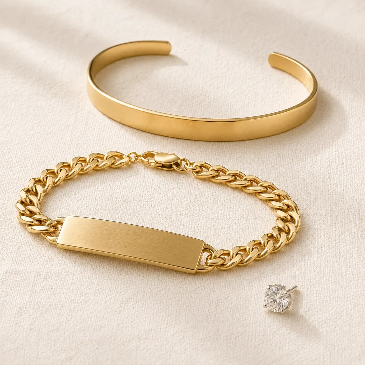 Men's cuff bracelet, ID bracelet, and single diamond stud earring on cream linen at ATL Luxury Jewelers Atlanta