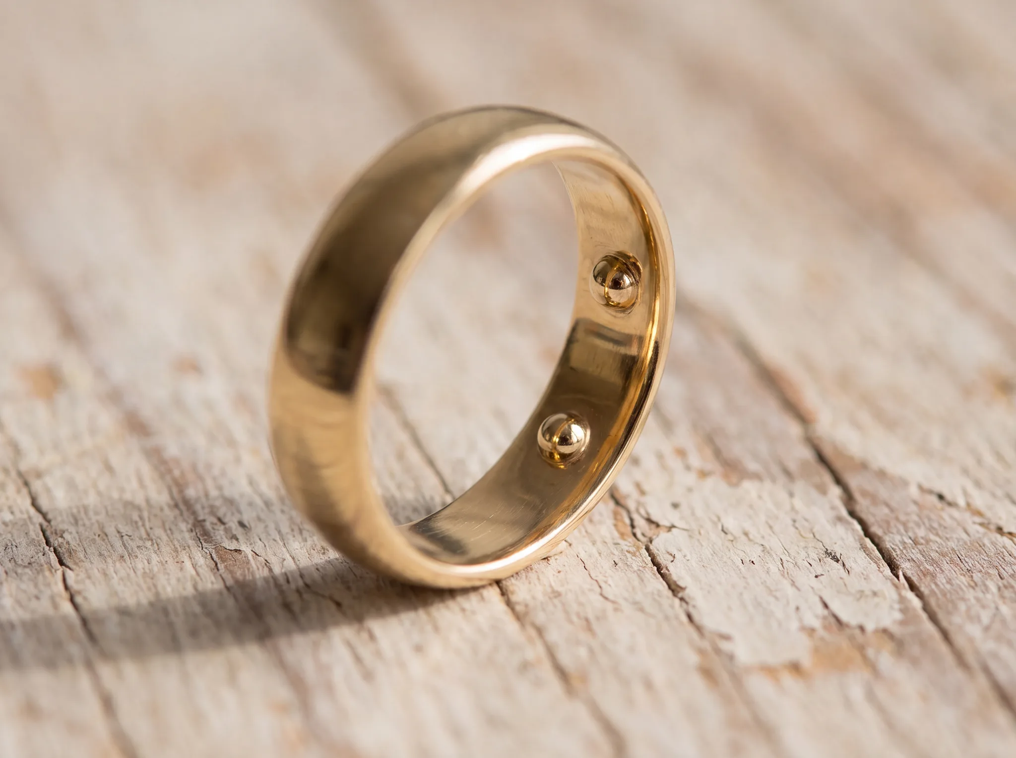 A yellow gold ring tilted on pale weathered oak to show the inside of its shank, with two small round gold beads soldered opposite each other on the inner wall.