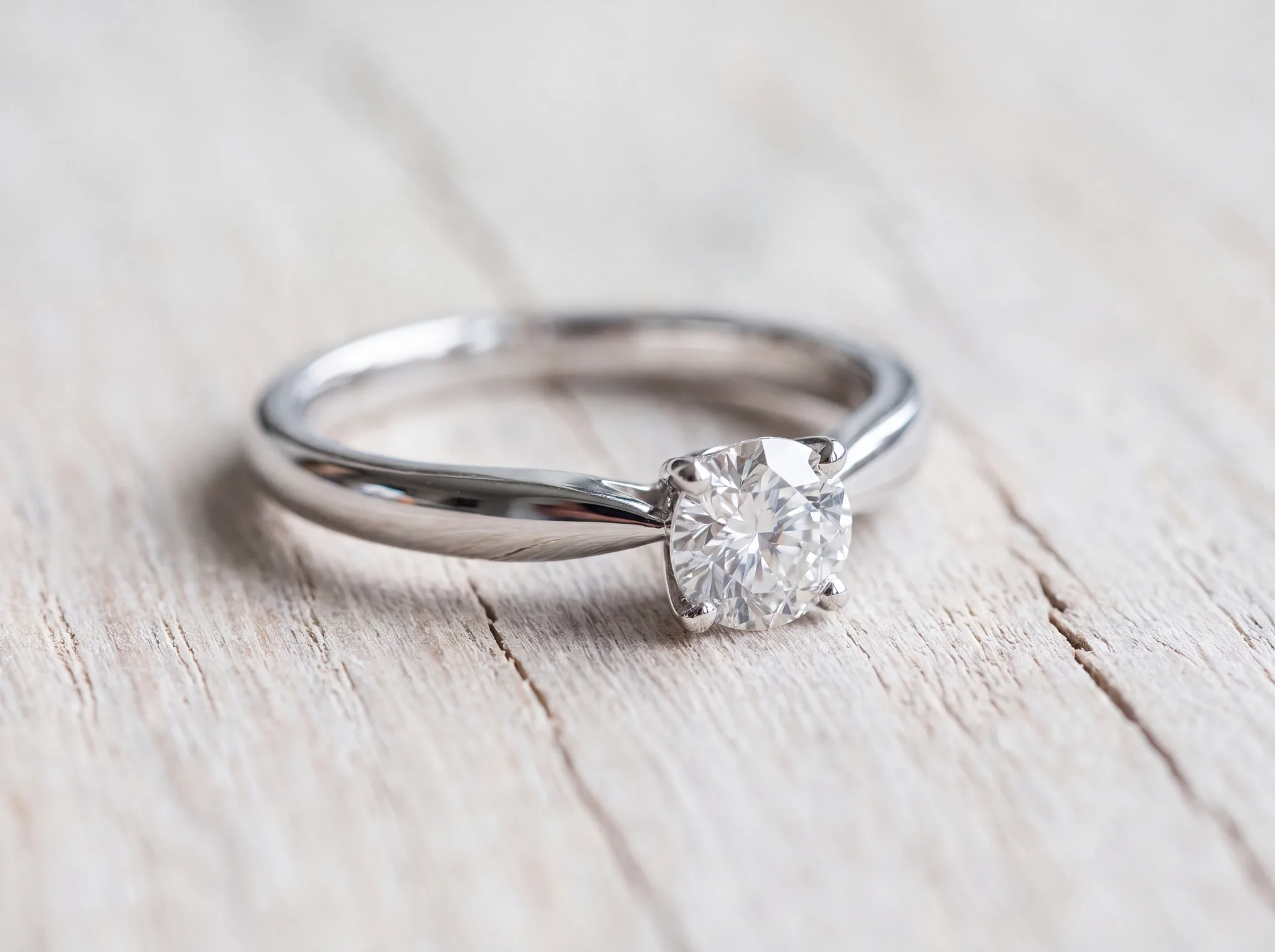 A white gold diamond ring on a pale wood surface, uniformly bright cool white across the band, shoulders and setting after a fresh rhodium plating
