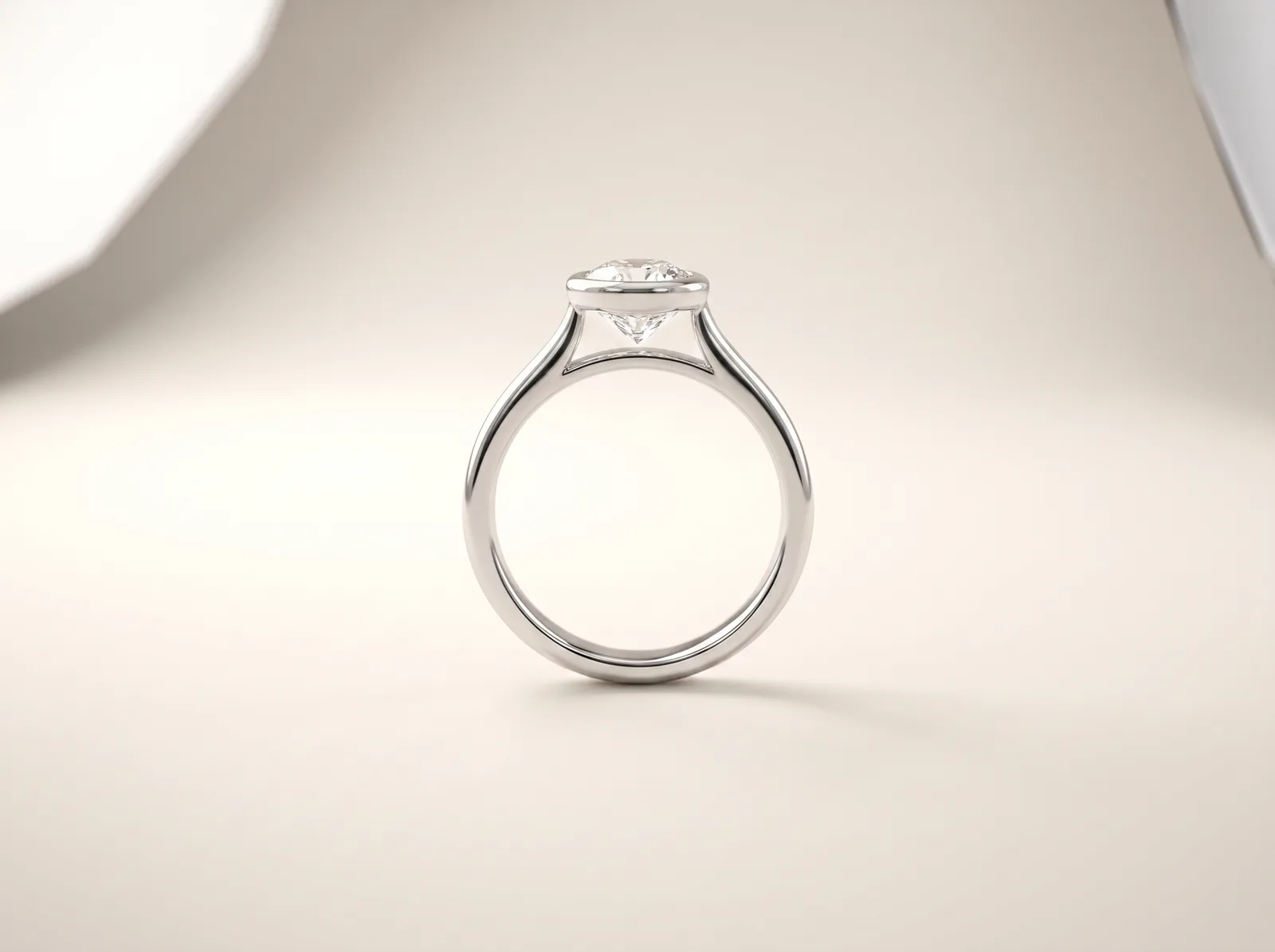 A platinum bezel-set engagement ring standing upright: a round diamond held by a continuous low rim of metal, with no prongs and nothing standing proud of the band.