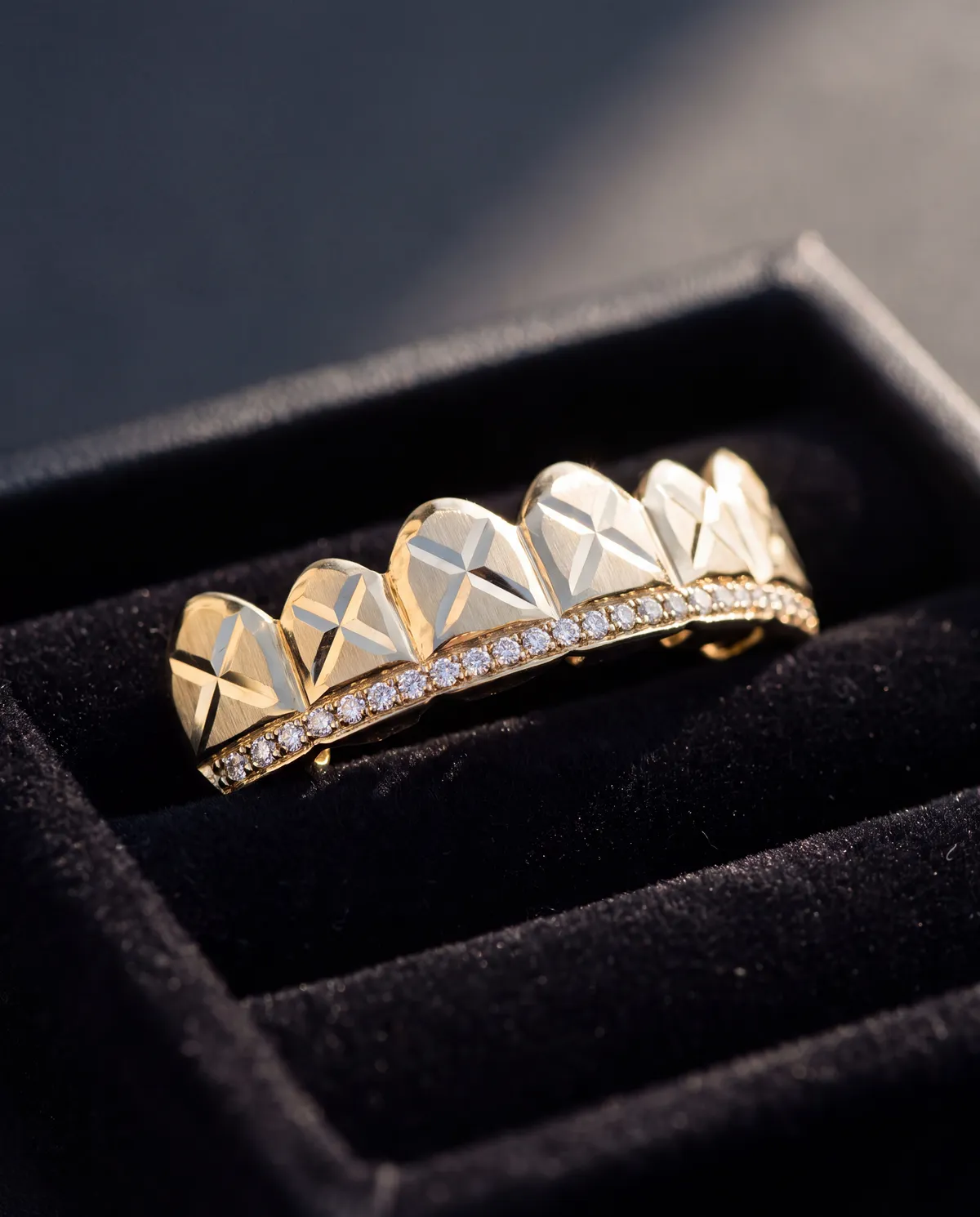 A gold grillz piece with a row of pavé diamonds along the bottom edge, displayed in an open jewelry box