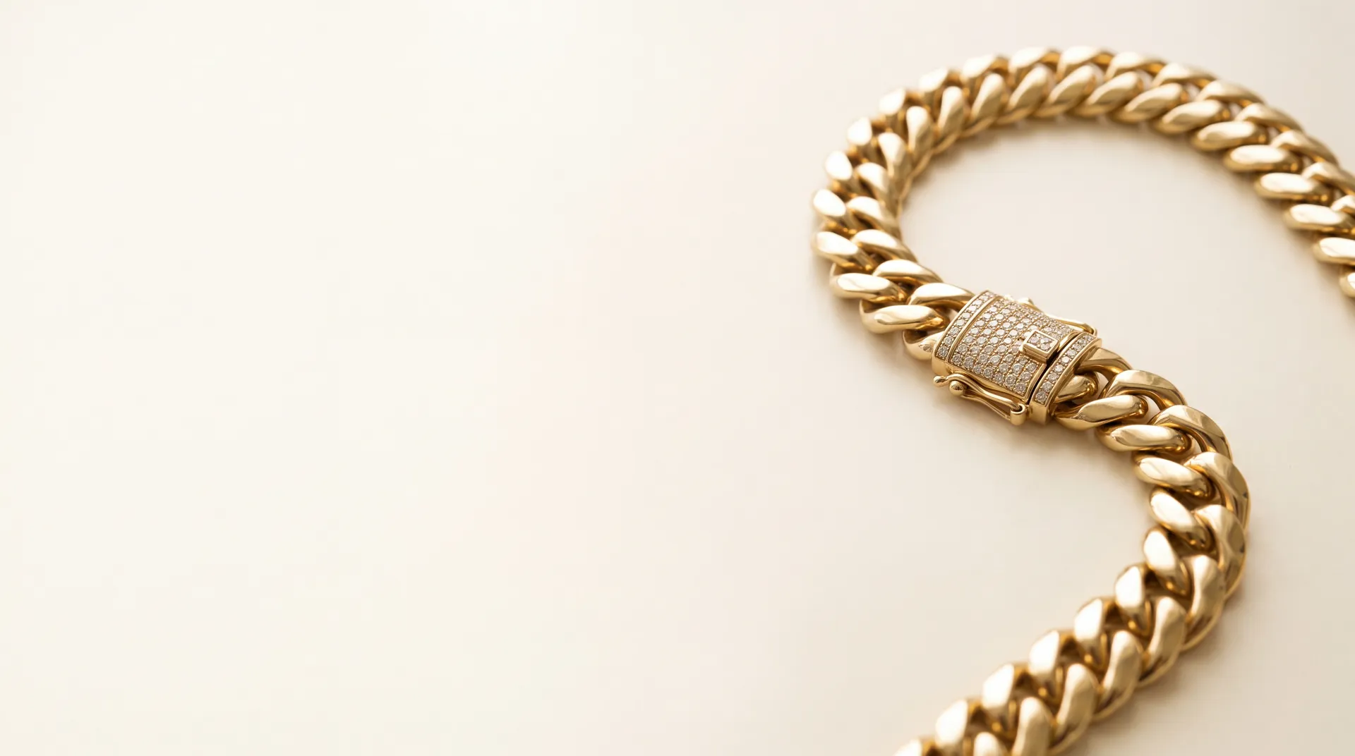 A coiled 14K yellow gold Cuban link chain with a pavé diamond clasp, shown on a plain cream background