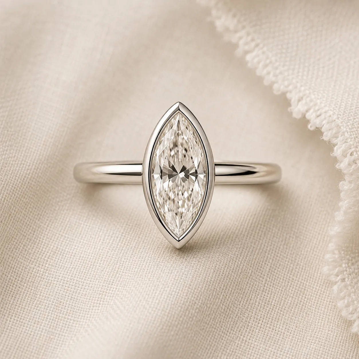 Bezel-set marquise diamond engagement ring with continuous platinum rim on cream linen