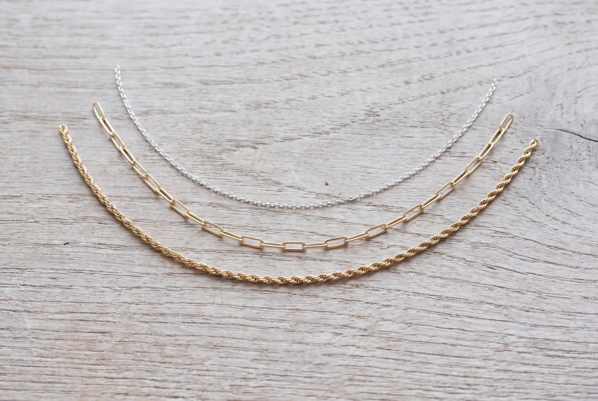 Three chains of different thickness laid on oak, silver next to gold