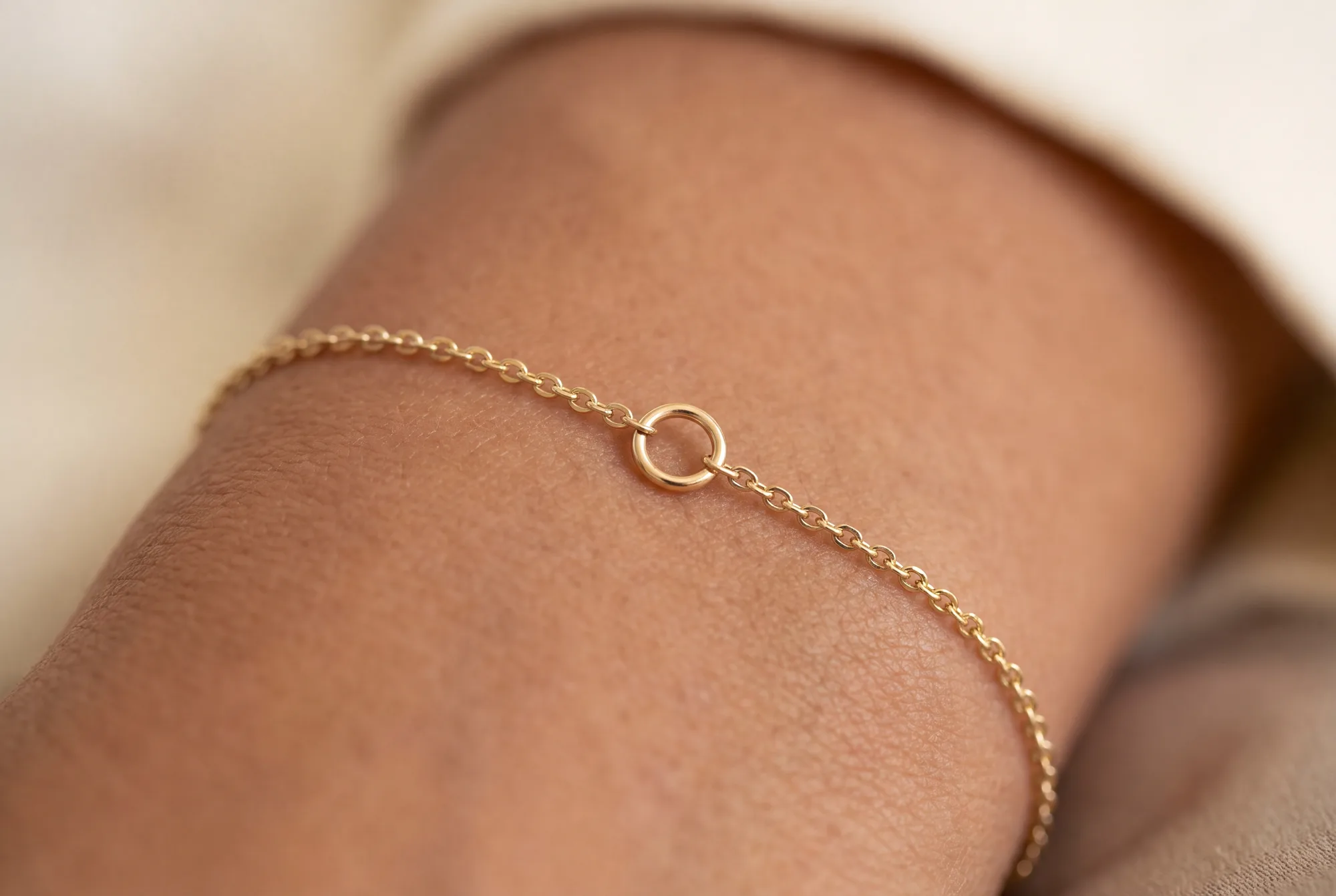 A tiny closed jump ring joining a fine gold chain on a wrist