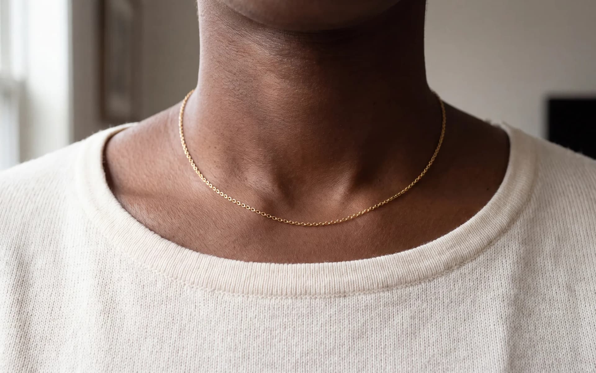 A short fine necklace resting at the base of the neck, cropped below the chin.