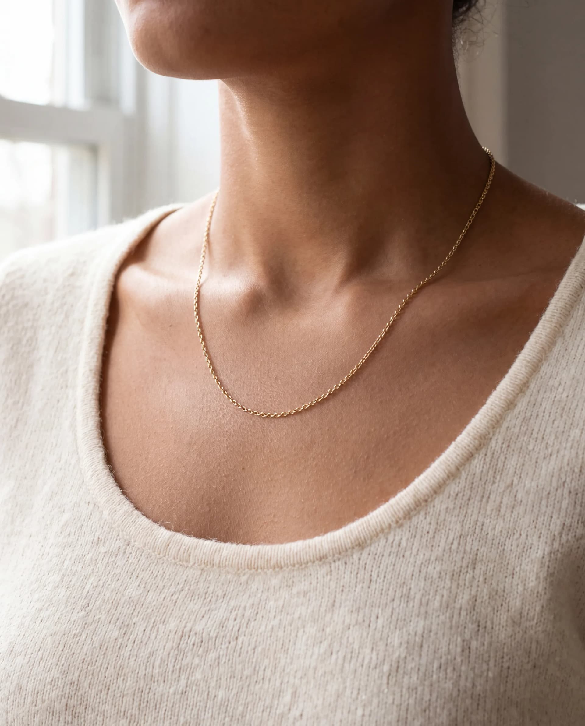 A collarbone and neckline wearing a fine 14K gold cable necklace over a cream knit top