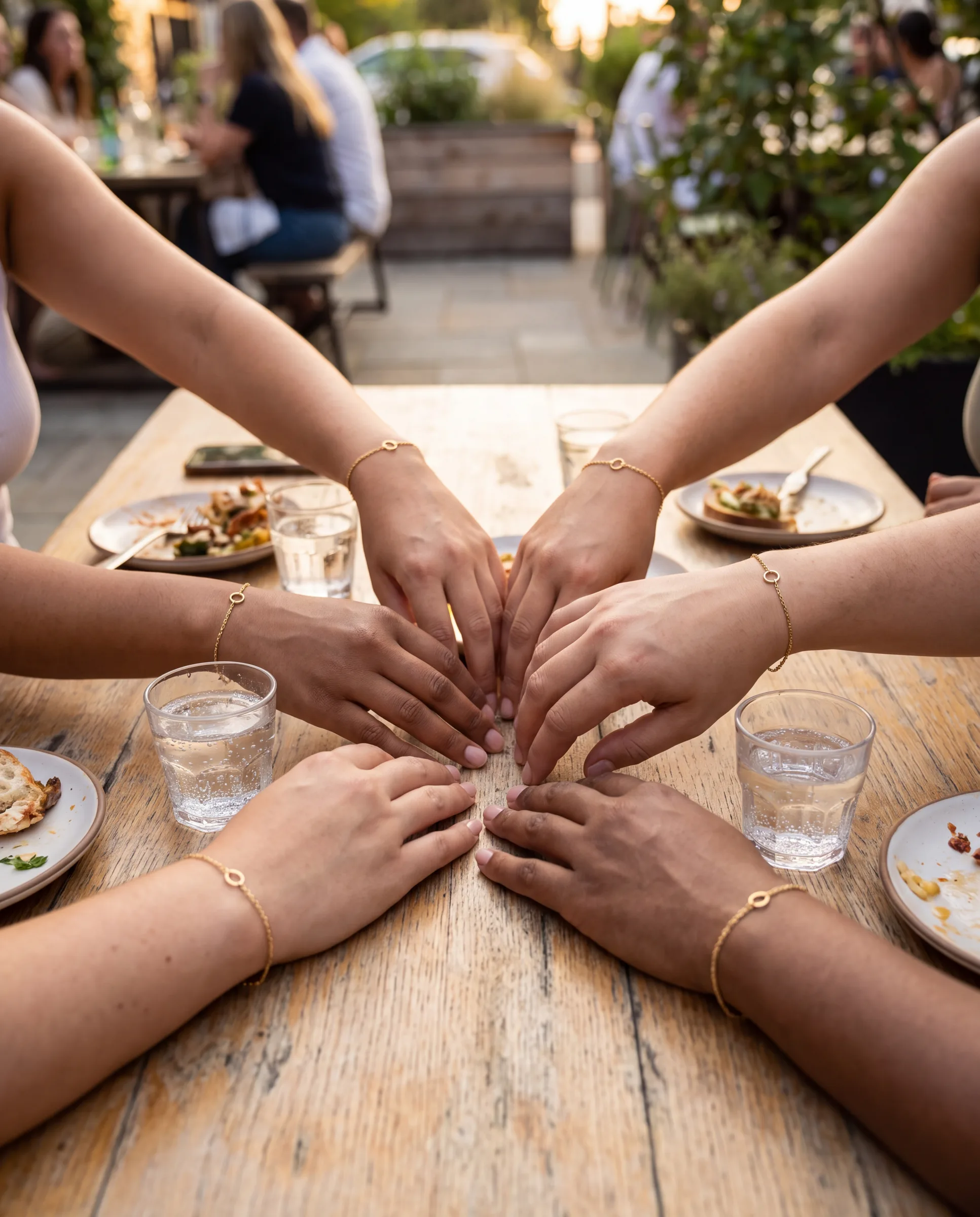 Several hands around a table with small glasses of sparkling water, each wearing a fresh fine bracelet