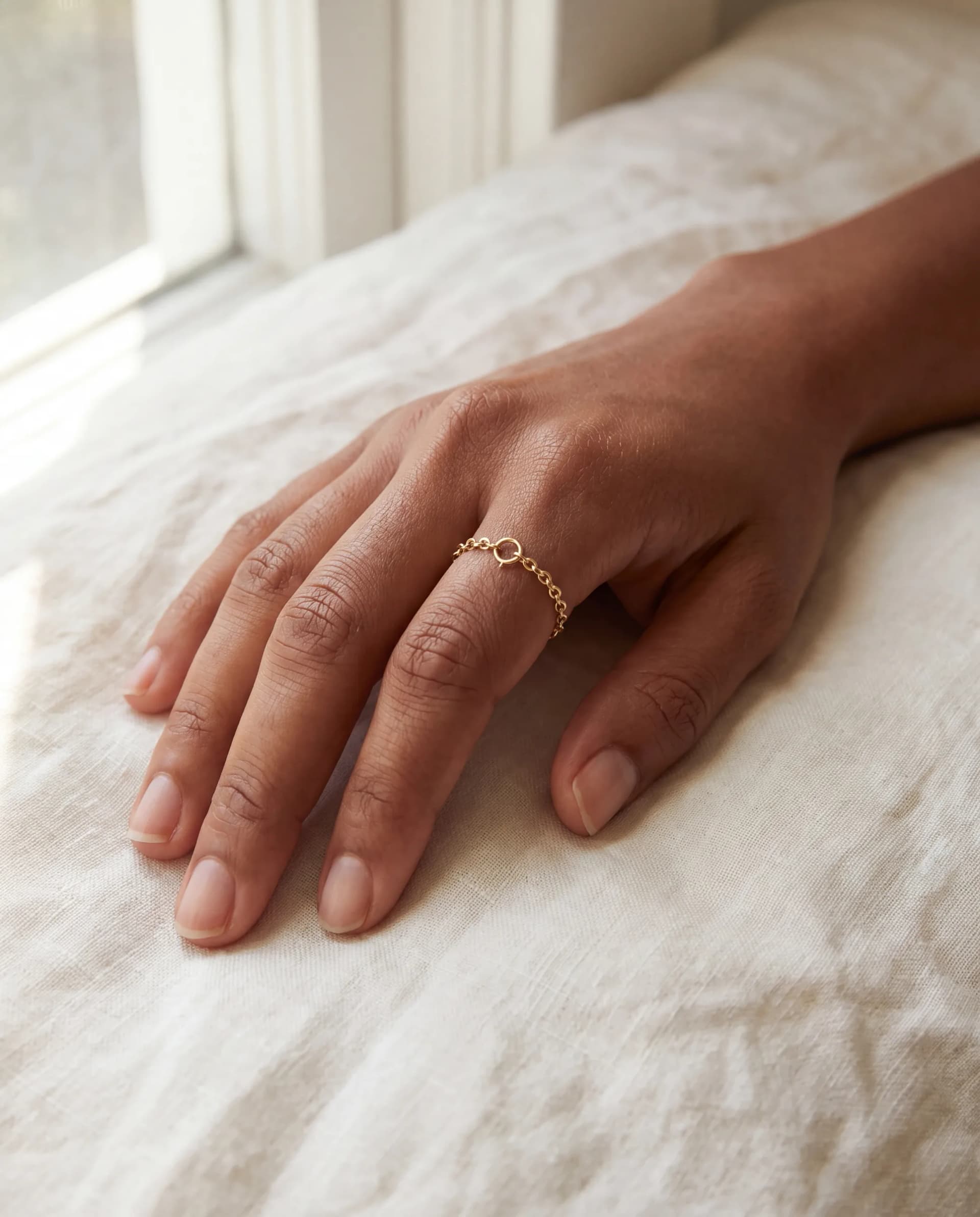 A hand resting on linen with a fine welded chain ring on the index finger