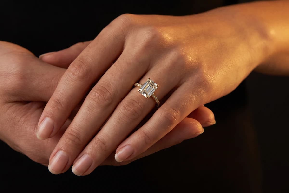 Design prototype — a rendering of an emerald-cut diamond ring with a pavé diamond band, worn on the ring finger of one hand resting over another, a piece ATL Luxury Jewelry can make for you.