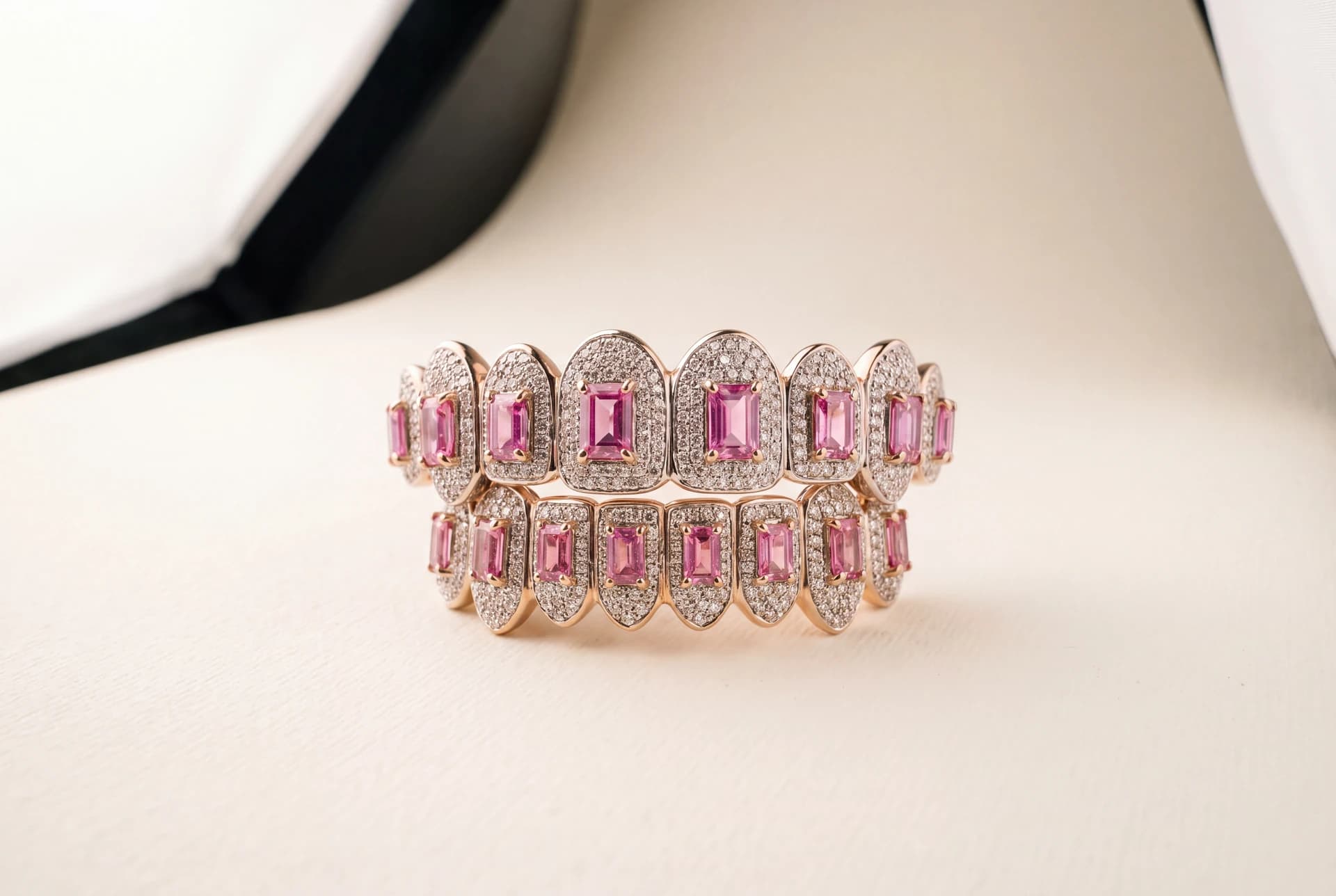 A fully-iced yellow gold custom grillz set with pink gemstones, top and bottom, on a cream backdrop.