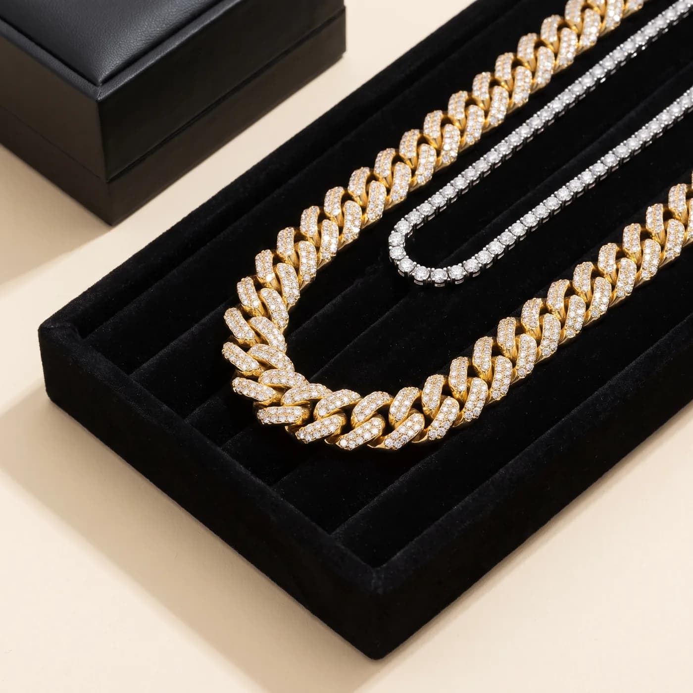 An iced gold Cuban link chain and a diamond tennis chain in a jeweller’s velvet tray