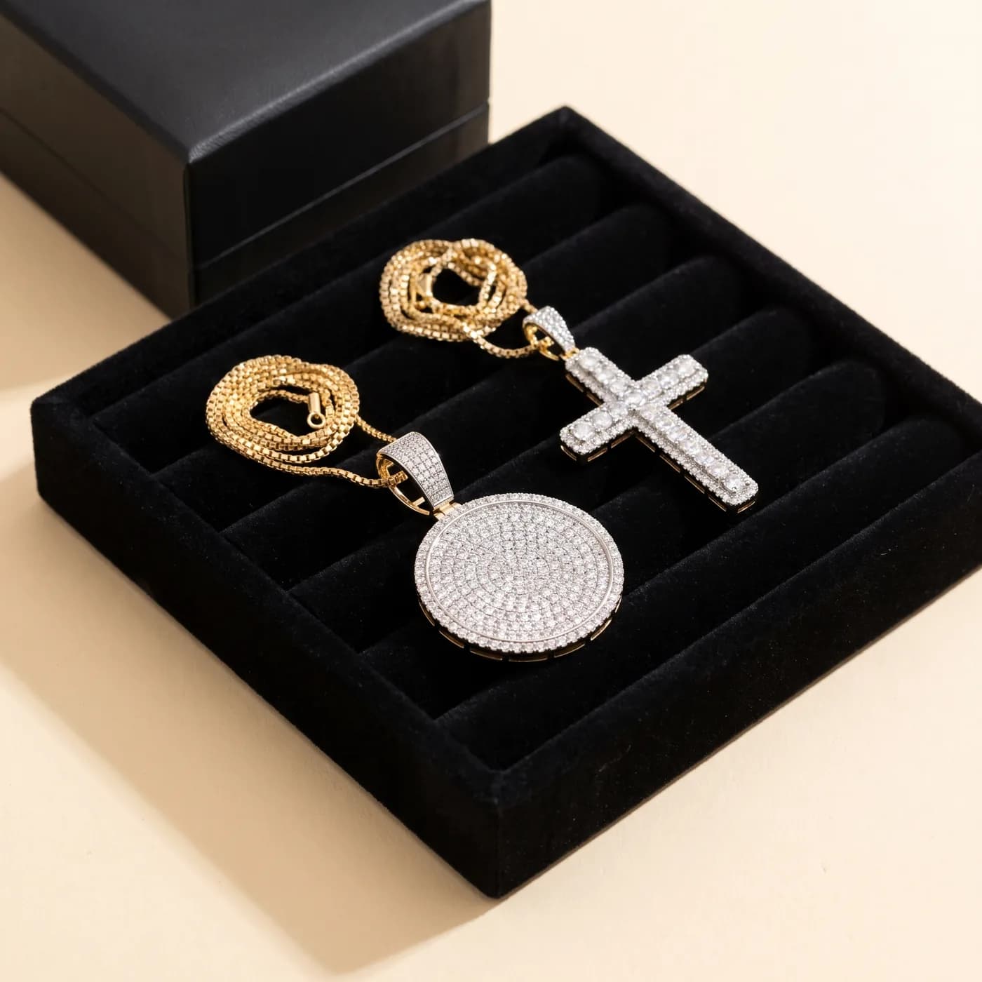 A pavé diamond medallion pendant and a pavé diamond cross pendant on gold chains, in a jeweller’s velvet tray