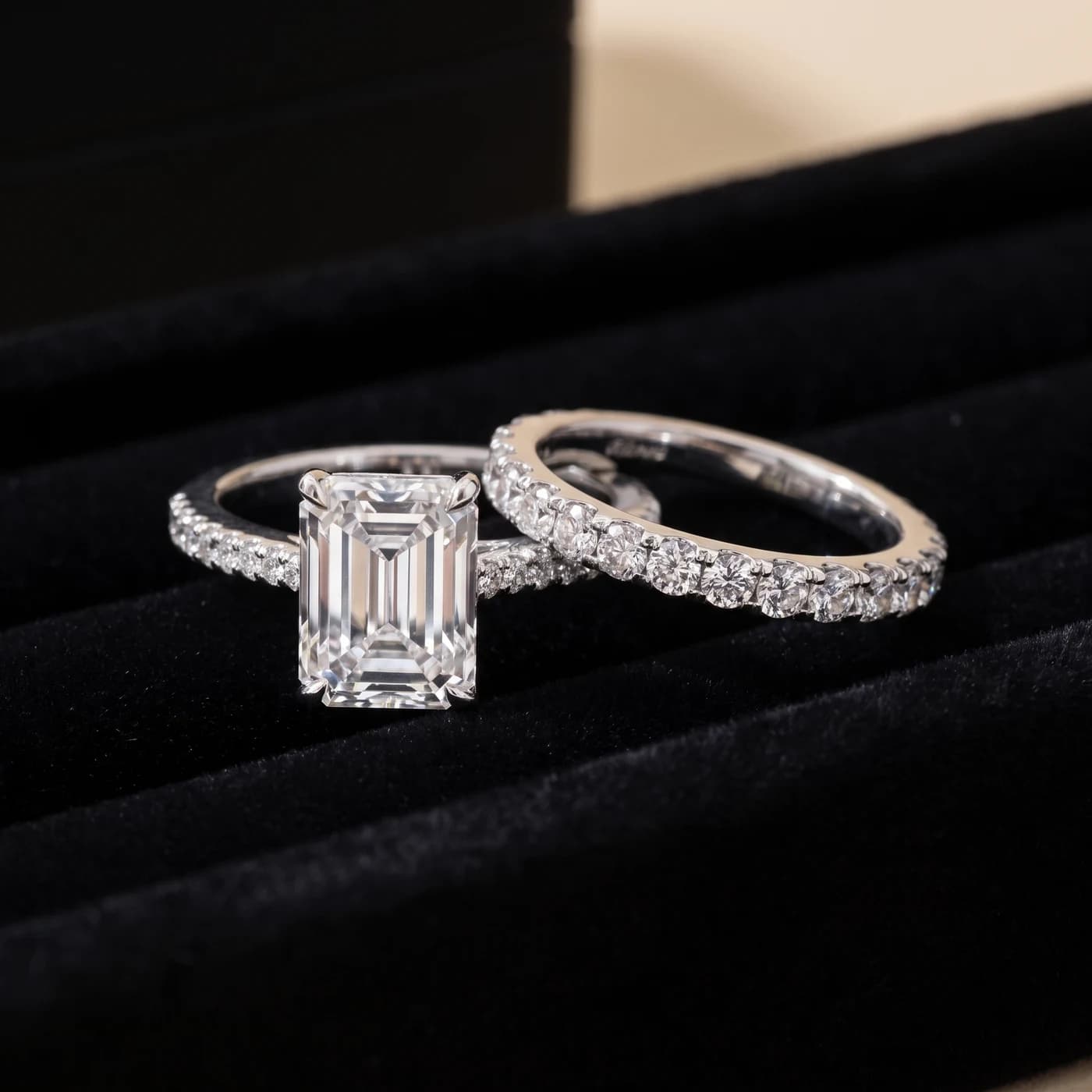 An emerald-cut diamond engagement ring beside its matching diamond eternity band, in a jeweller’s velvet tray