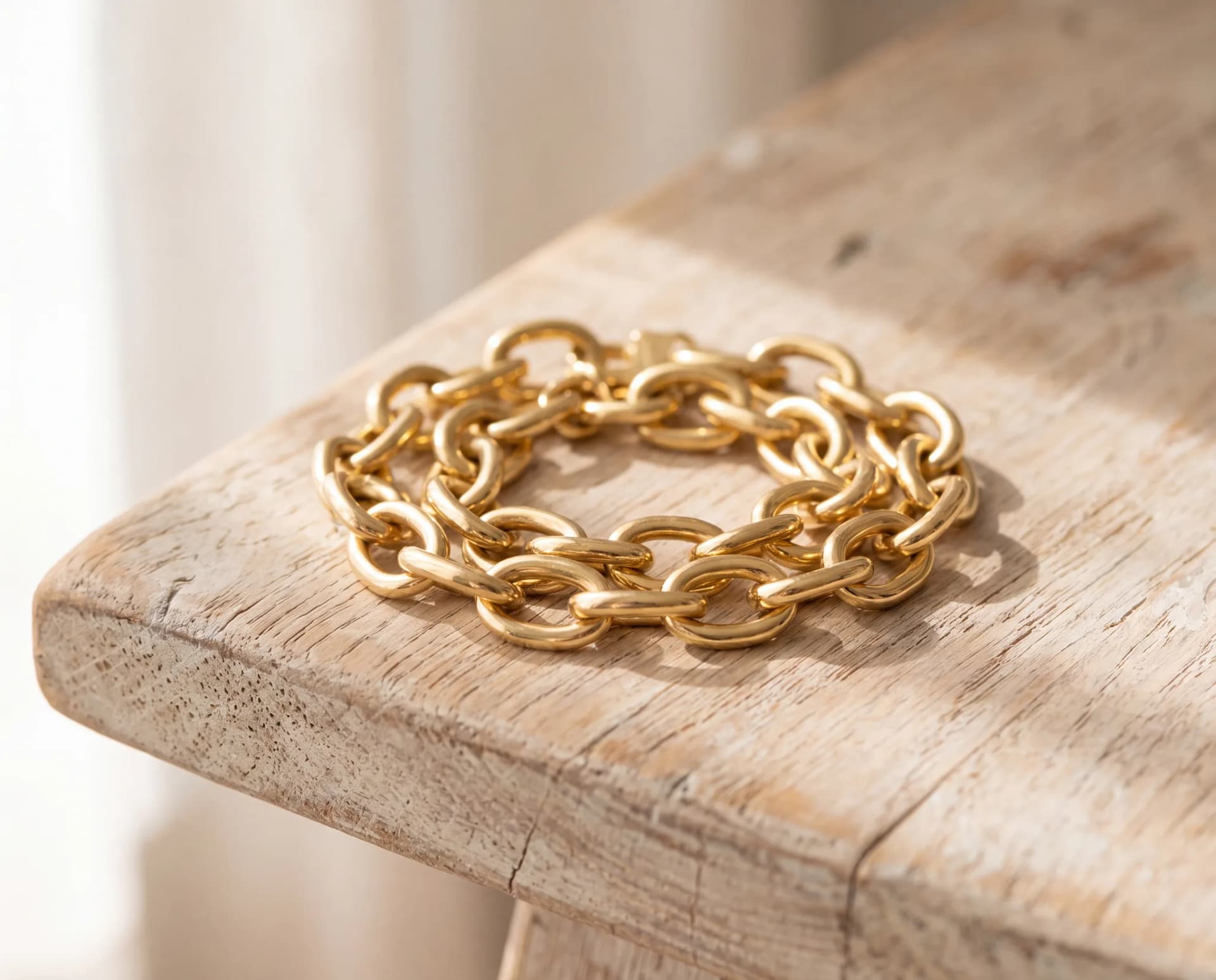A gold bracelet lying in a wide slack loop on a pale wood surface, clearly too large