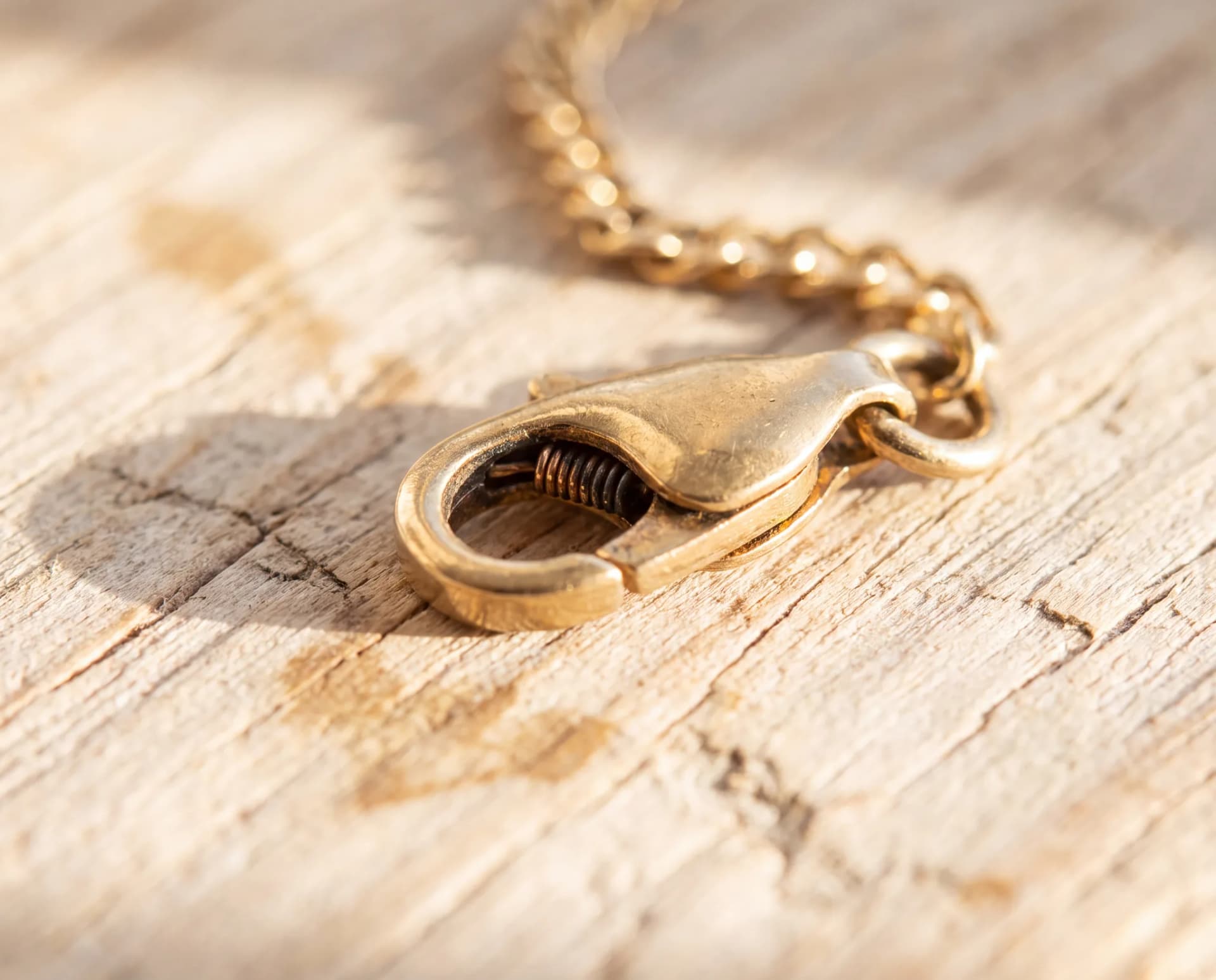 A chain's worn spring-ring clasp that will not close, resting on a pale wood surface
