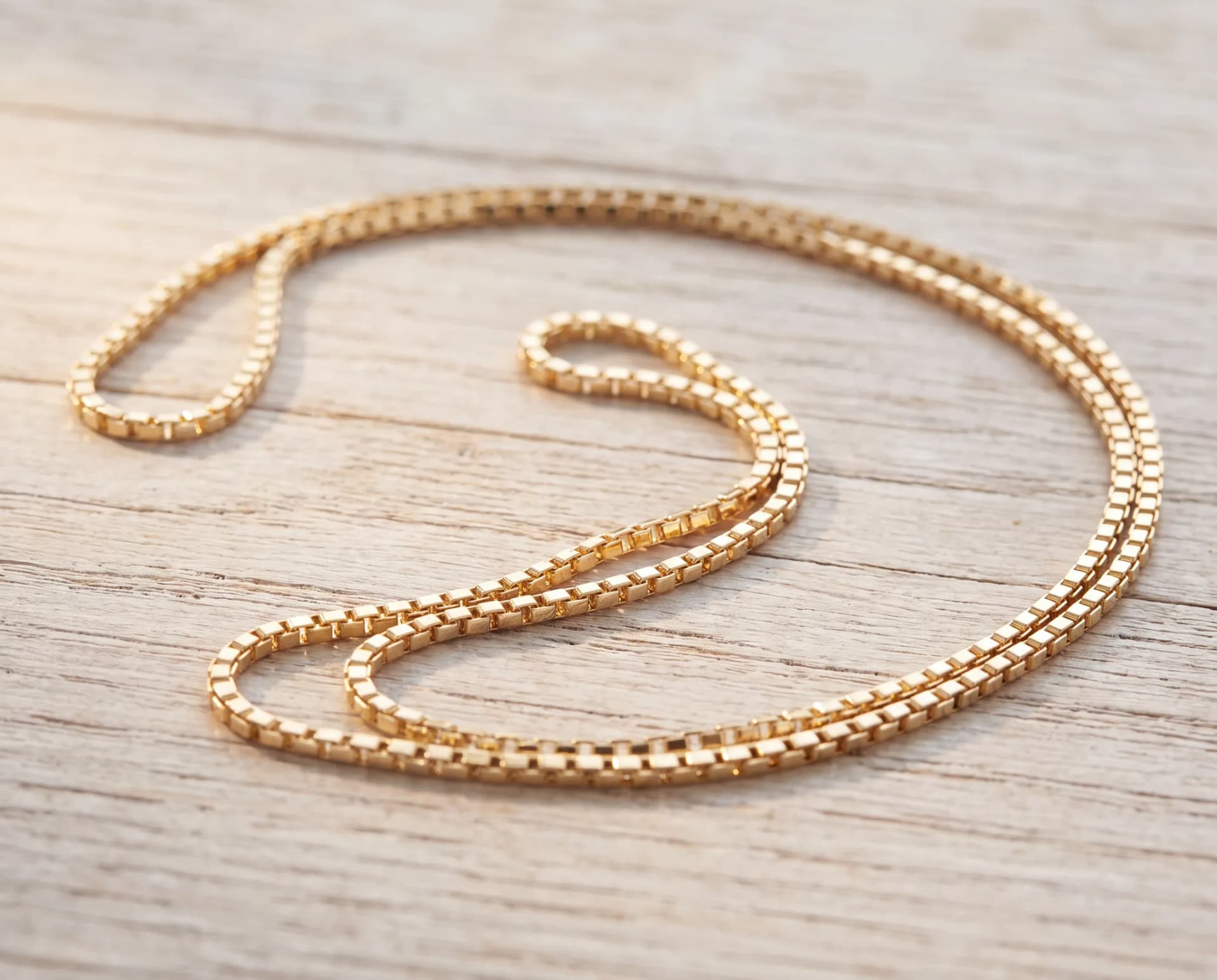 A long gold chain coiled on a pale wood surface, brought in to be shortened