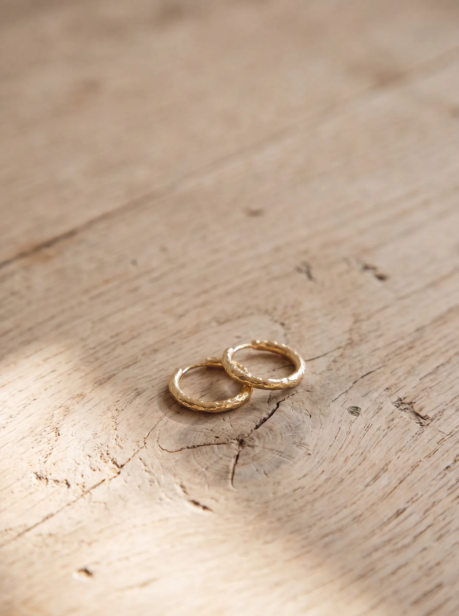 A pair of yellow gold earrings resting on a pale wood surface at ATL Luxury Jewelry, Snellville GA