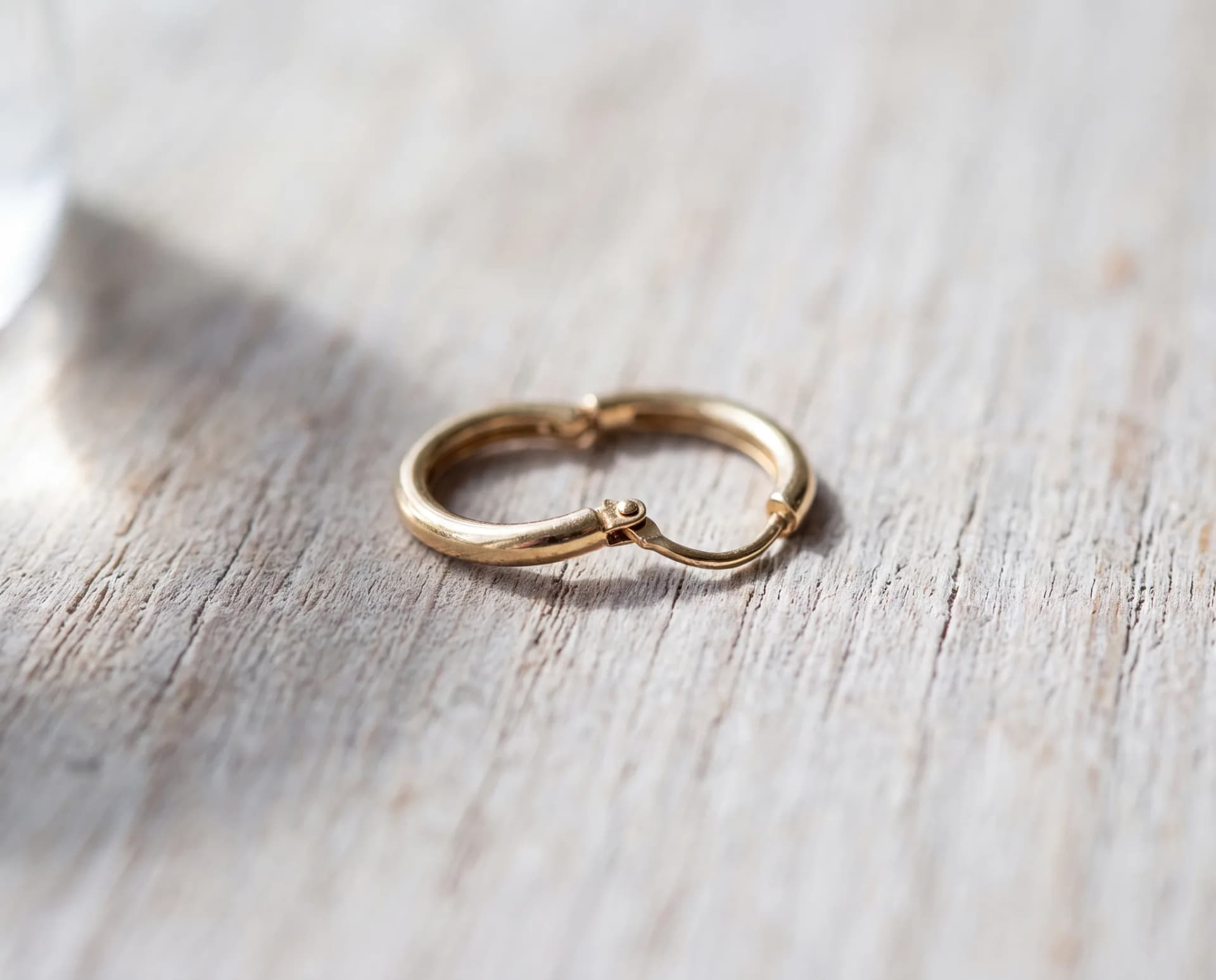 A gold hoop earring on a pale wood surface sprung open at its hinge