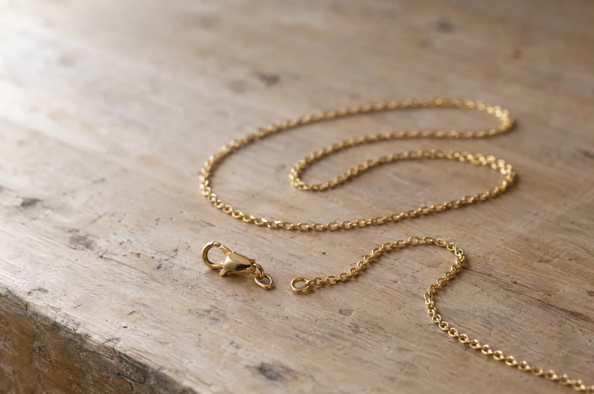 A gold chain resting on a plain wood surface, brought in for repair at ATL Luxury Jewelry, Snellville GA