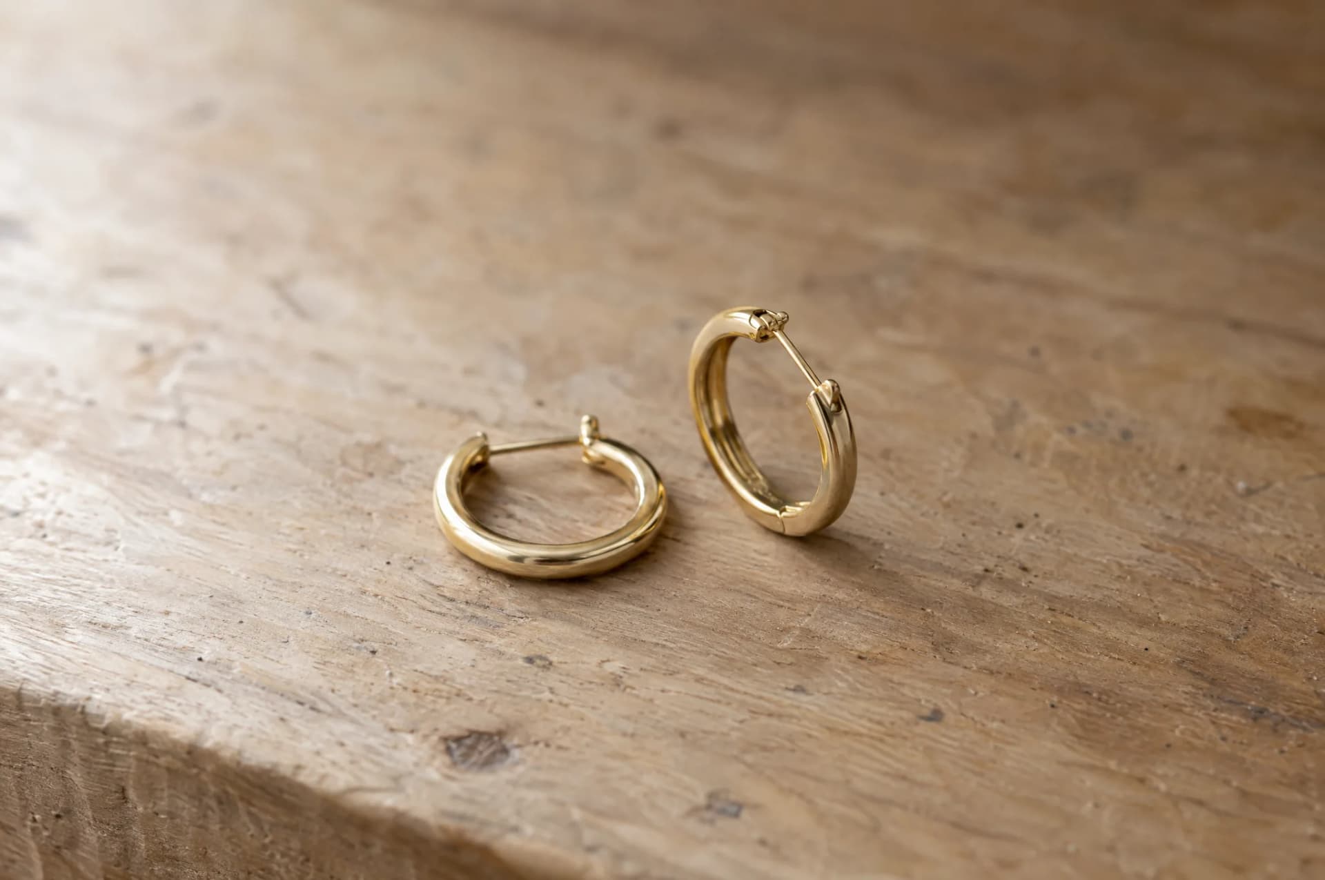 A pair of earrings resting on a plain wood surface, brought in for repair at ATL Luxury Jewelry, Snellville GA